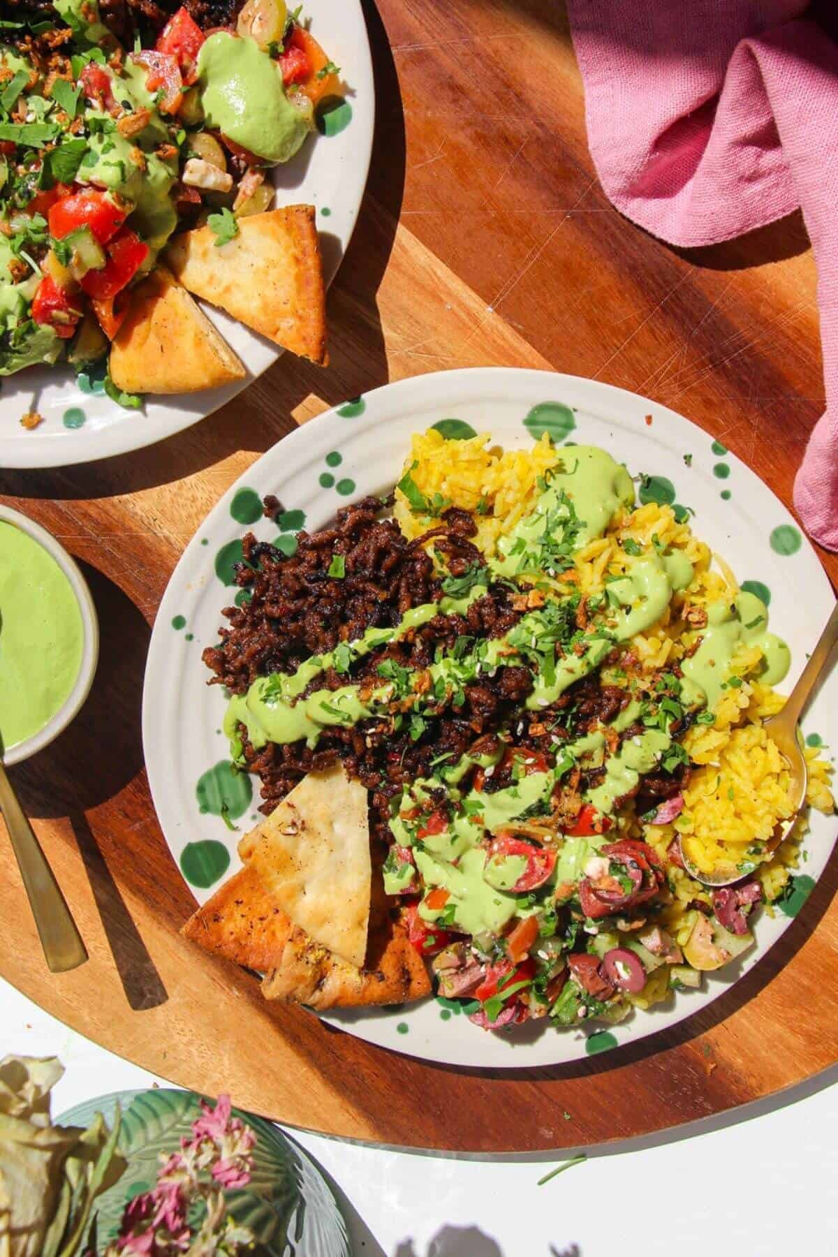 Two Mediterranean beef rice bowls, with green tahini sauce on the side.