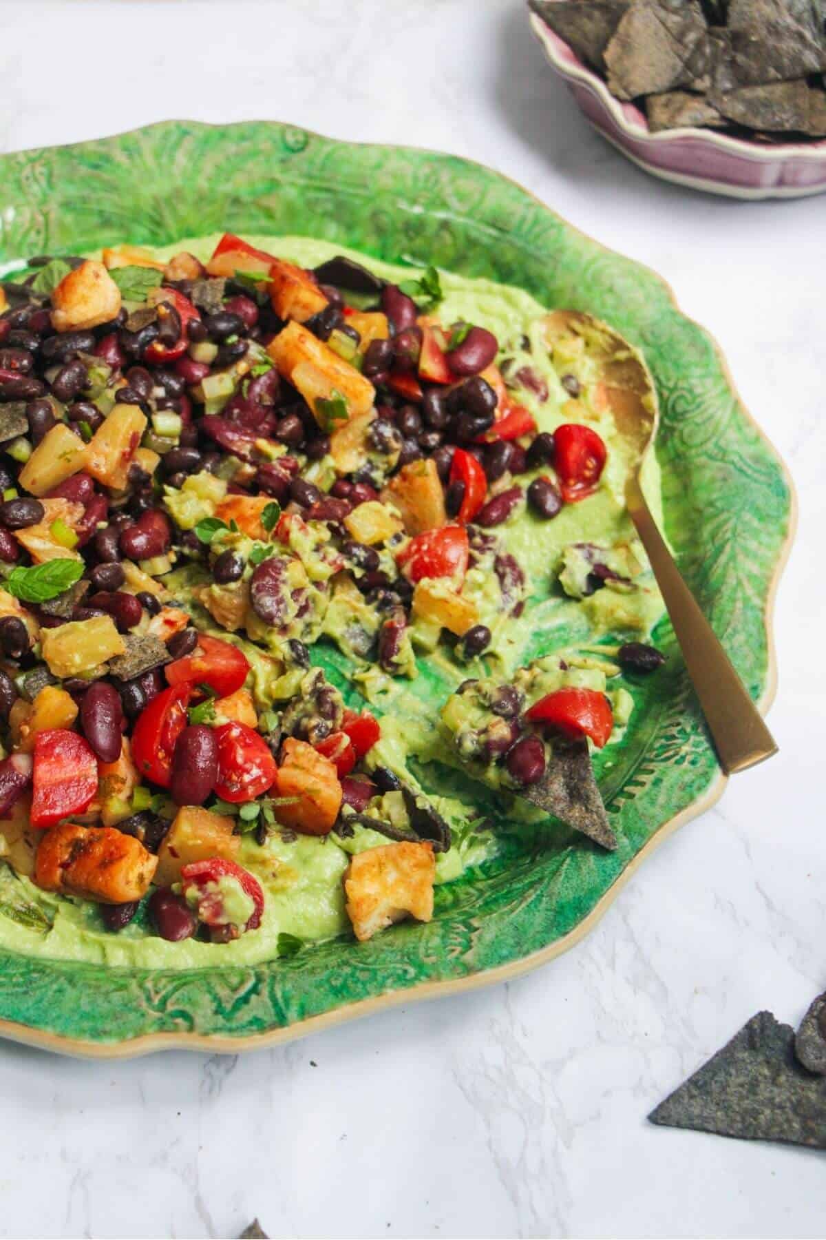 Mexican bean salad on top of whipped avocado on a large green platter.