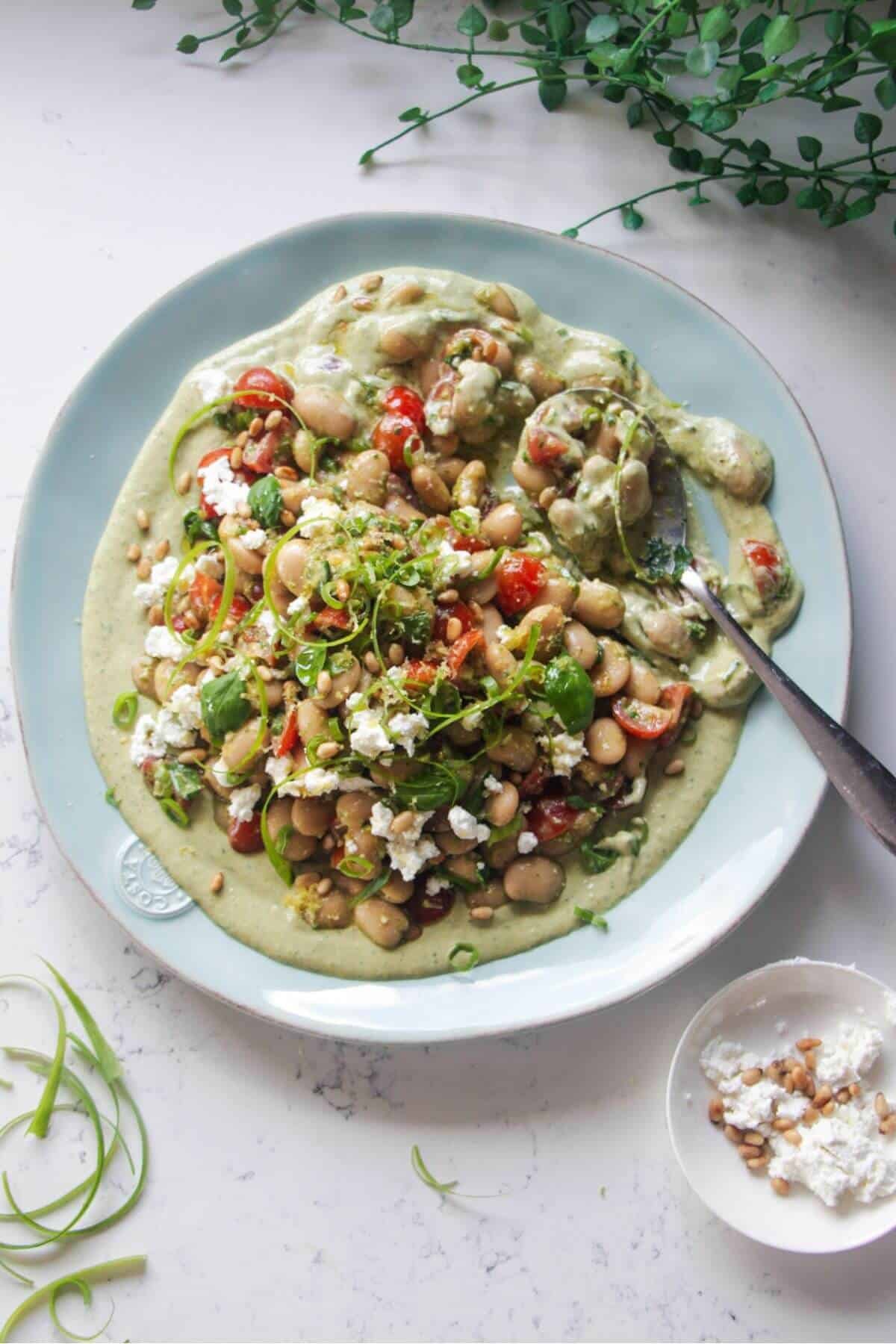 Mediterranean white bean salad on whipped basil tahini on a large light blue serving plate.
