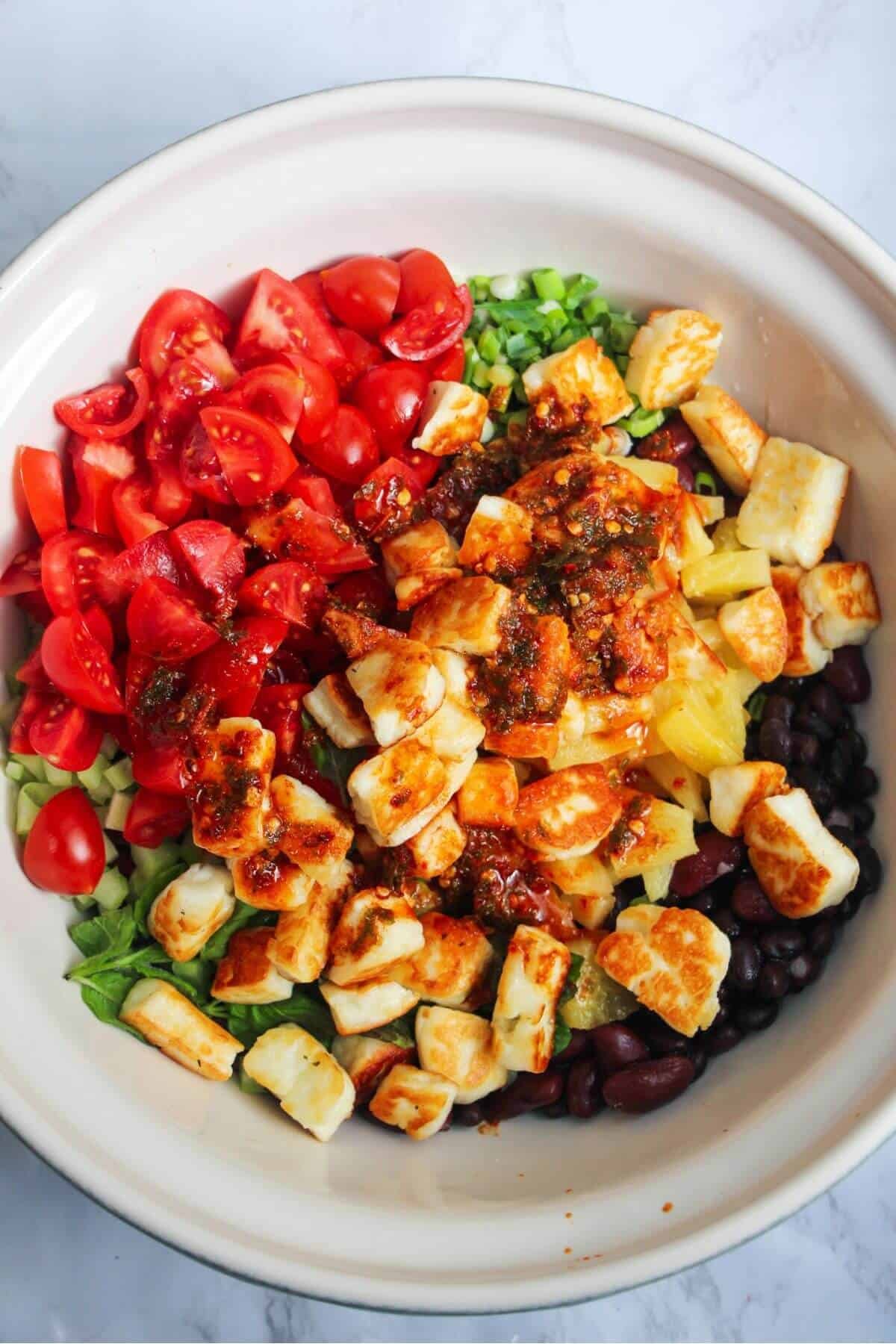 Chopped tomatoes, pan-fried halloumi, pineapple, scallions and celery in a large mixing bowl with black and Kidney beans.