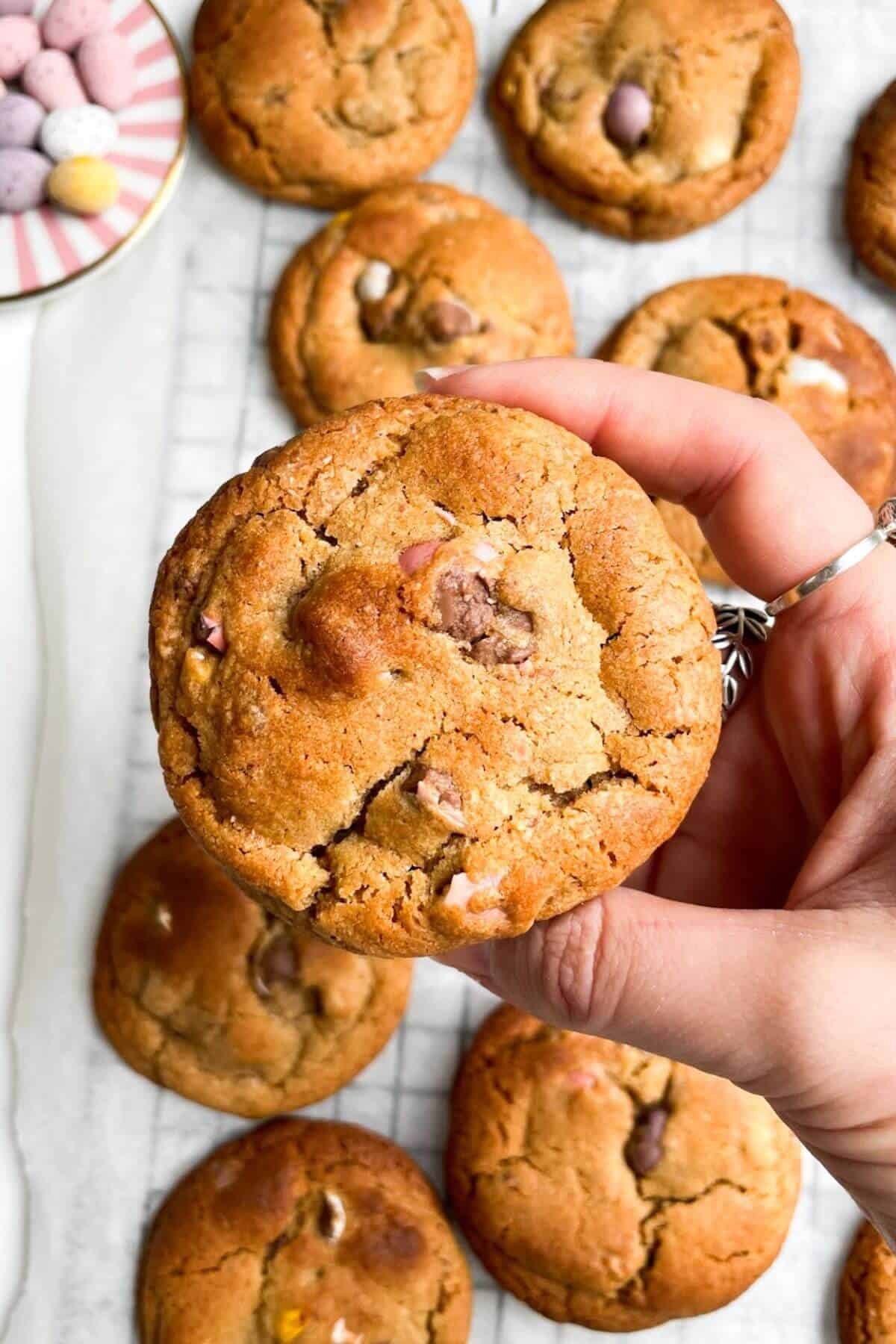 Hand holding up a mini egg cookie with more cookies in the background.