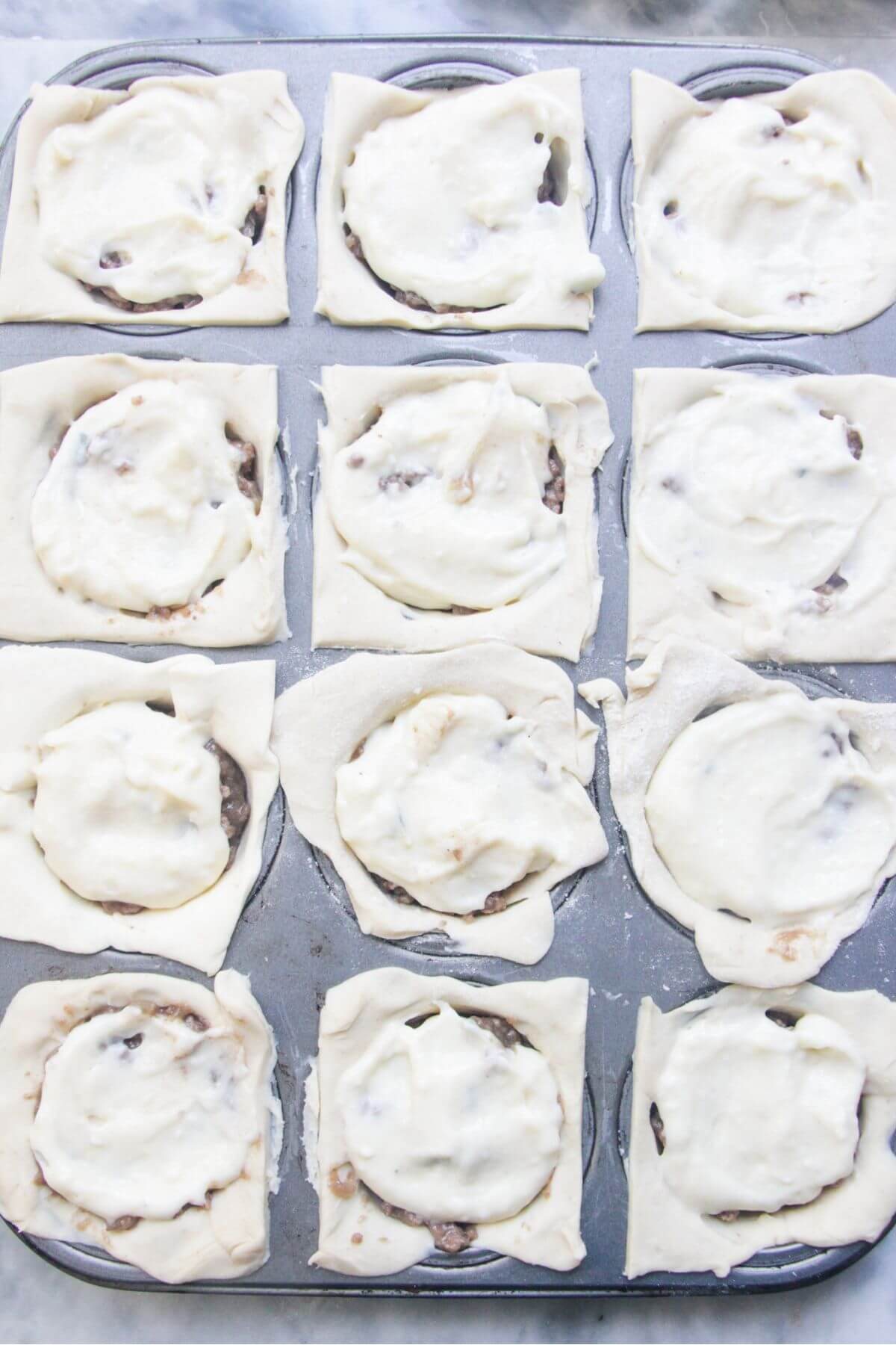 Cheesy béchamel sauce on top of mince in pastry in a 12 piece muffin tin.