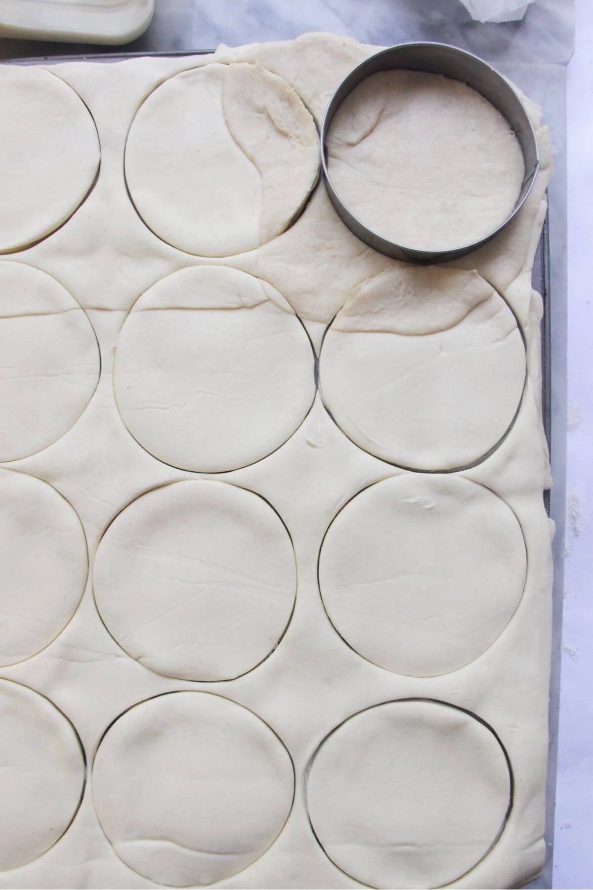 A silver cookie cutter sitting on top of pastry topped pies in a 12 piece muffin tin.