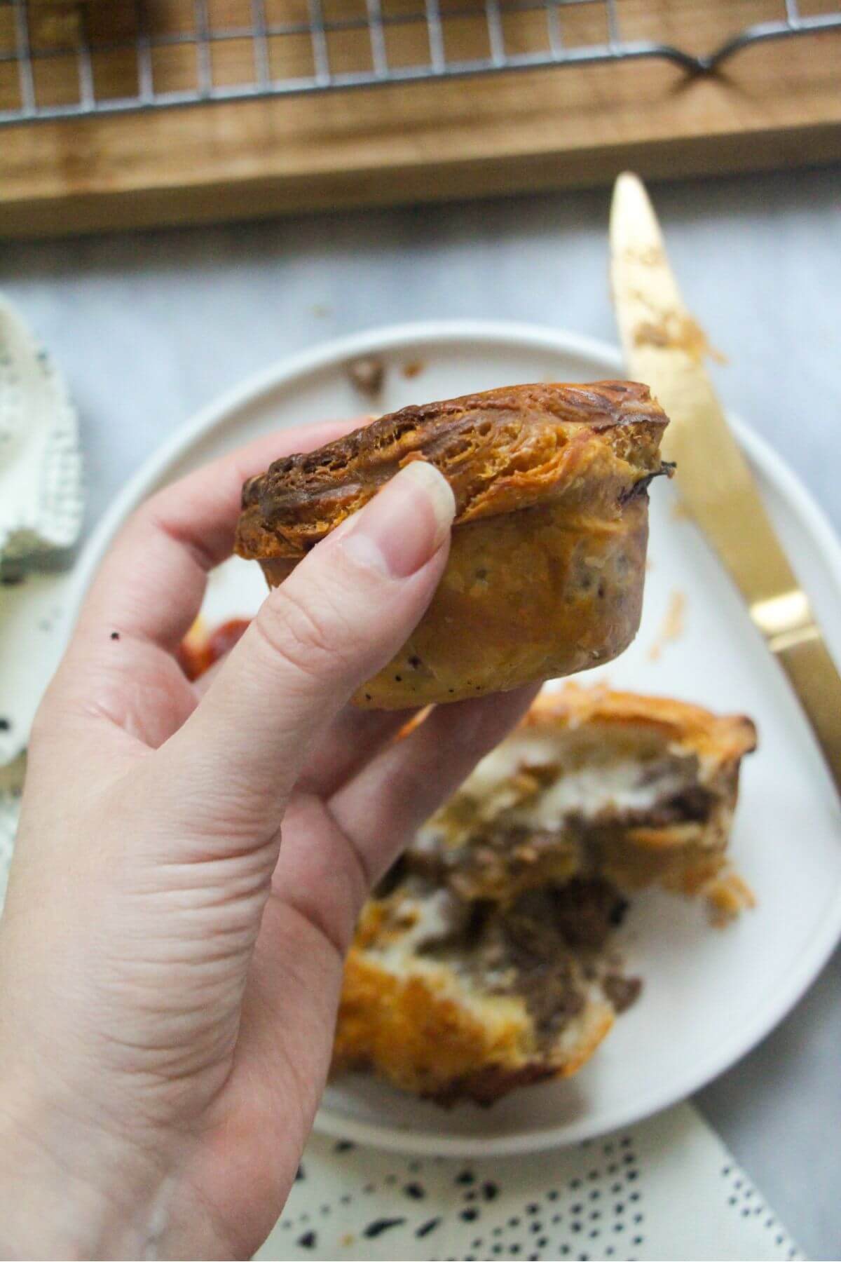 Close up of a hand holding up a small mince and cheese pie, looking at the side of a pie.