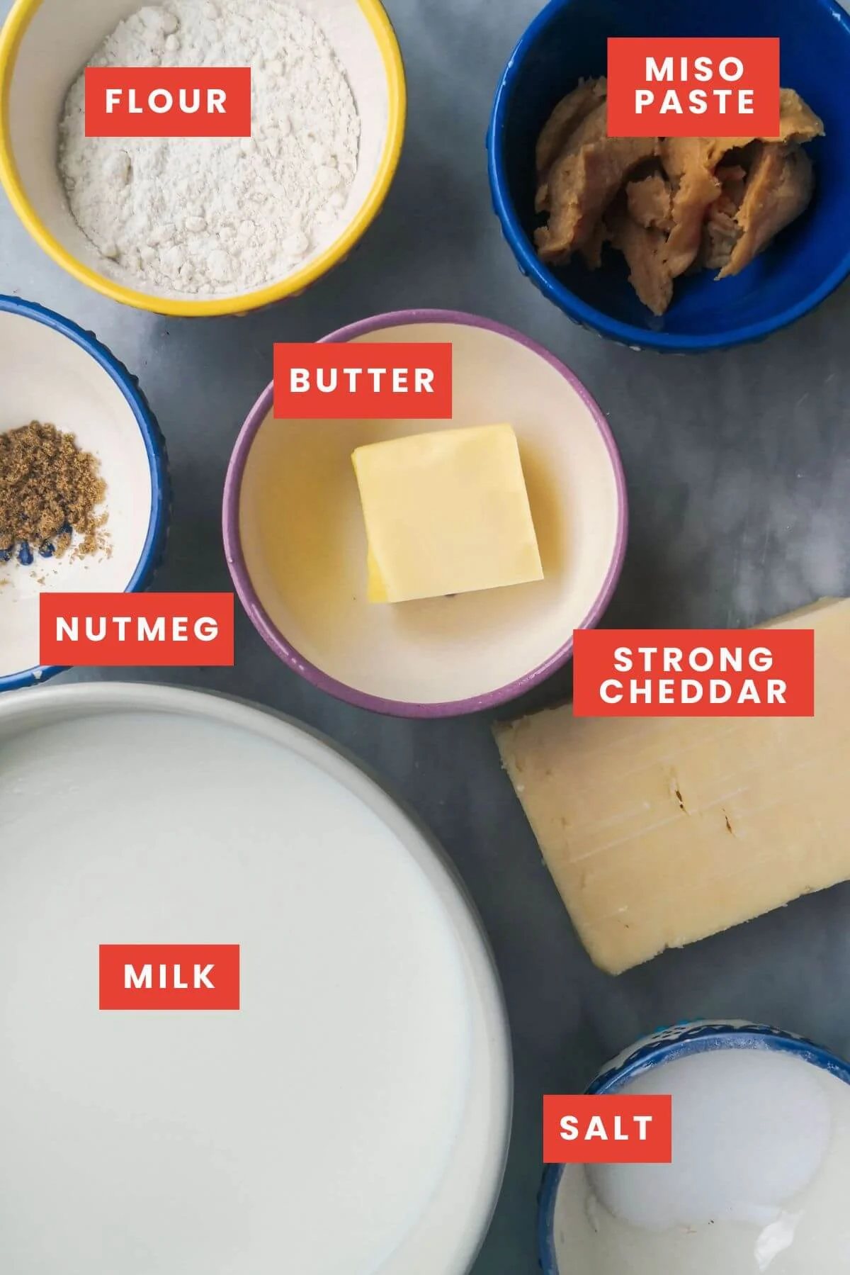 Cheesy béchamel sauce ingredients laid out on a marble background and labelled.