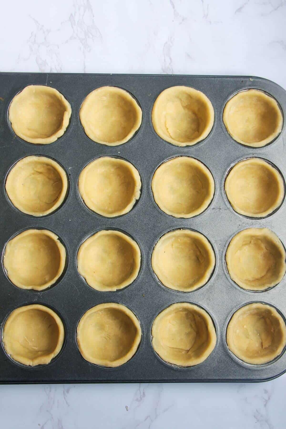Pastry pressing into mini muffin tin.