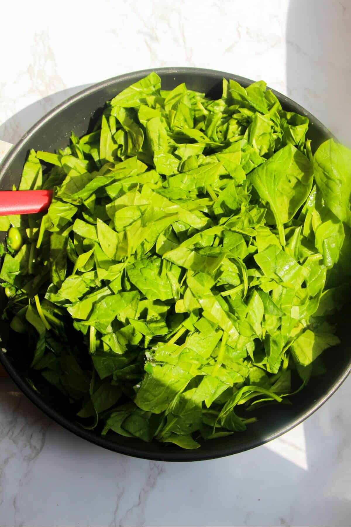 Spinach leaves piled into small frying pan.