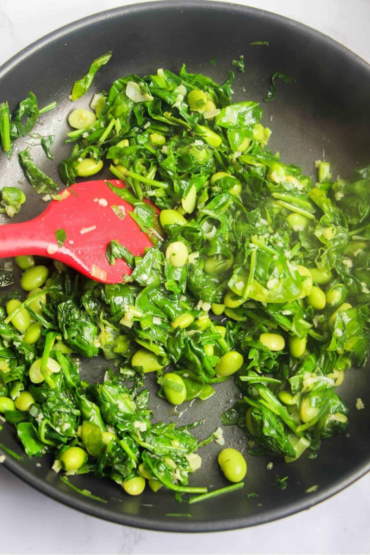 Spinach leaves wilted and cooked down in small frying pan.