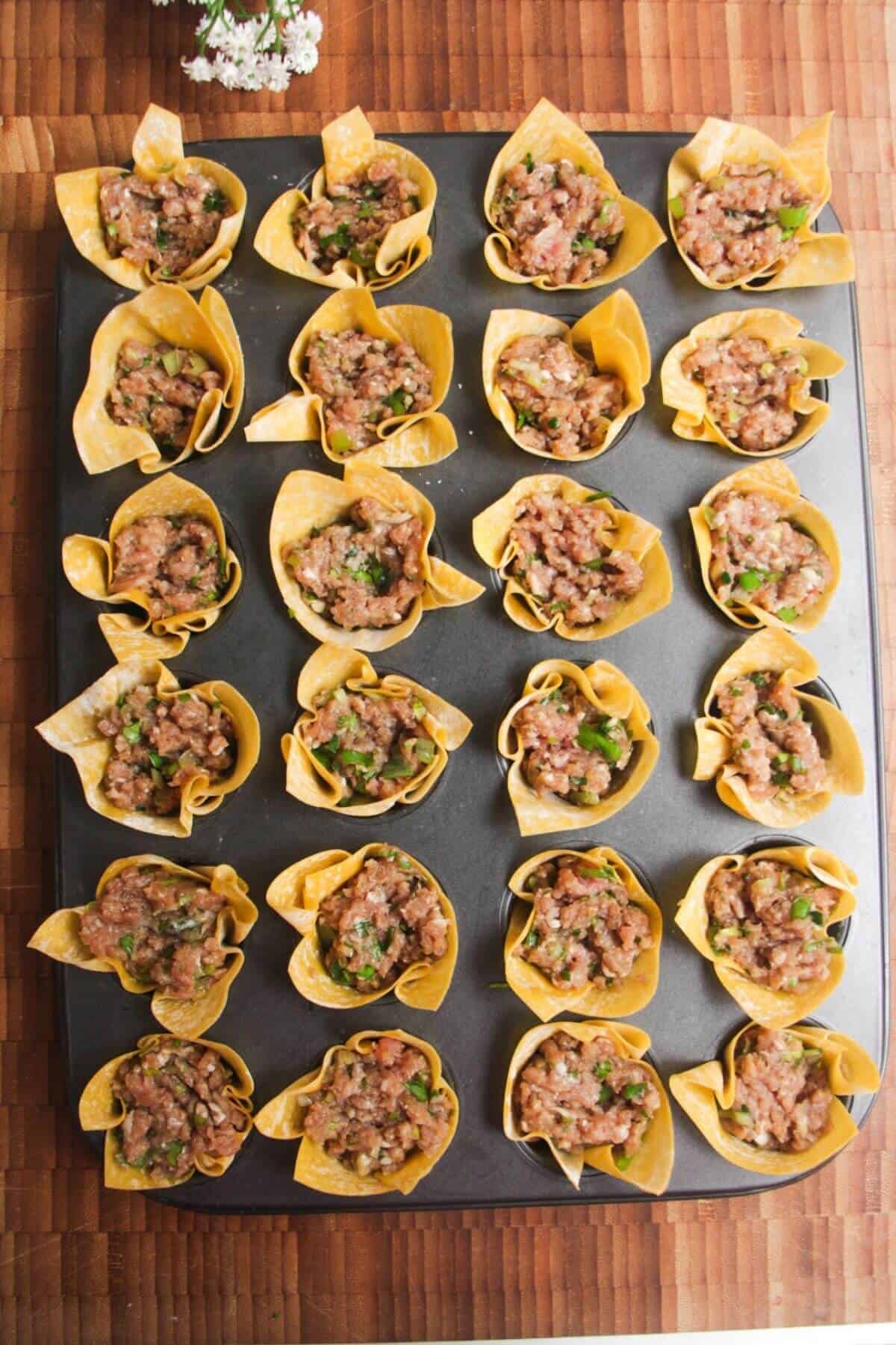 Dumpling filling in wonton cups in a mini muffin tin.