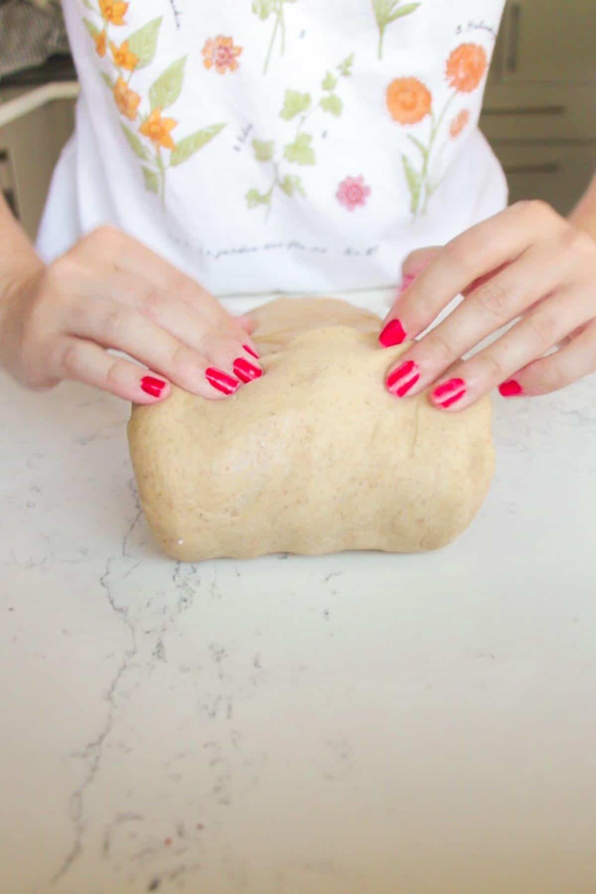 Rolling up mini egg hot cross bun dough on a white marble background.