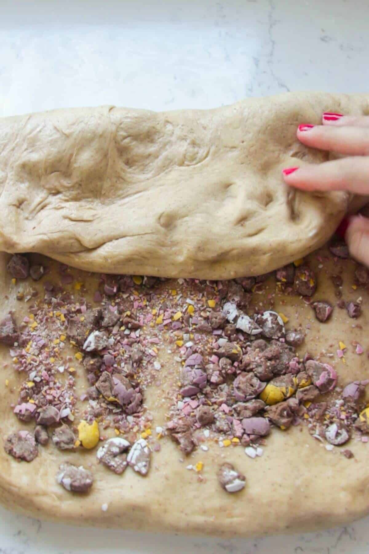 Hand folding mini egg studded dough over itself.