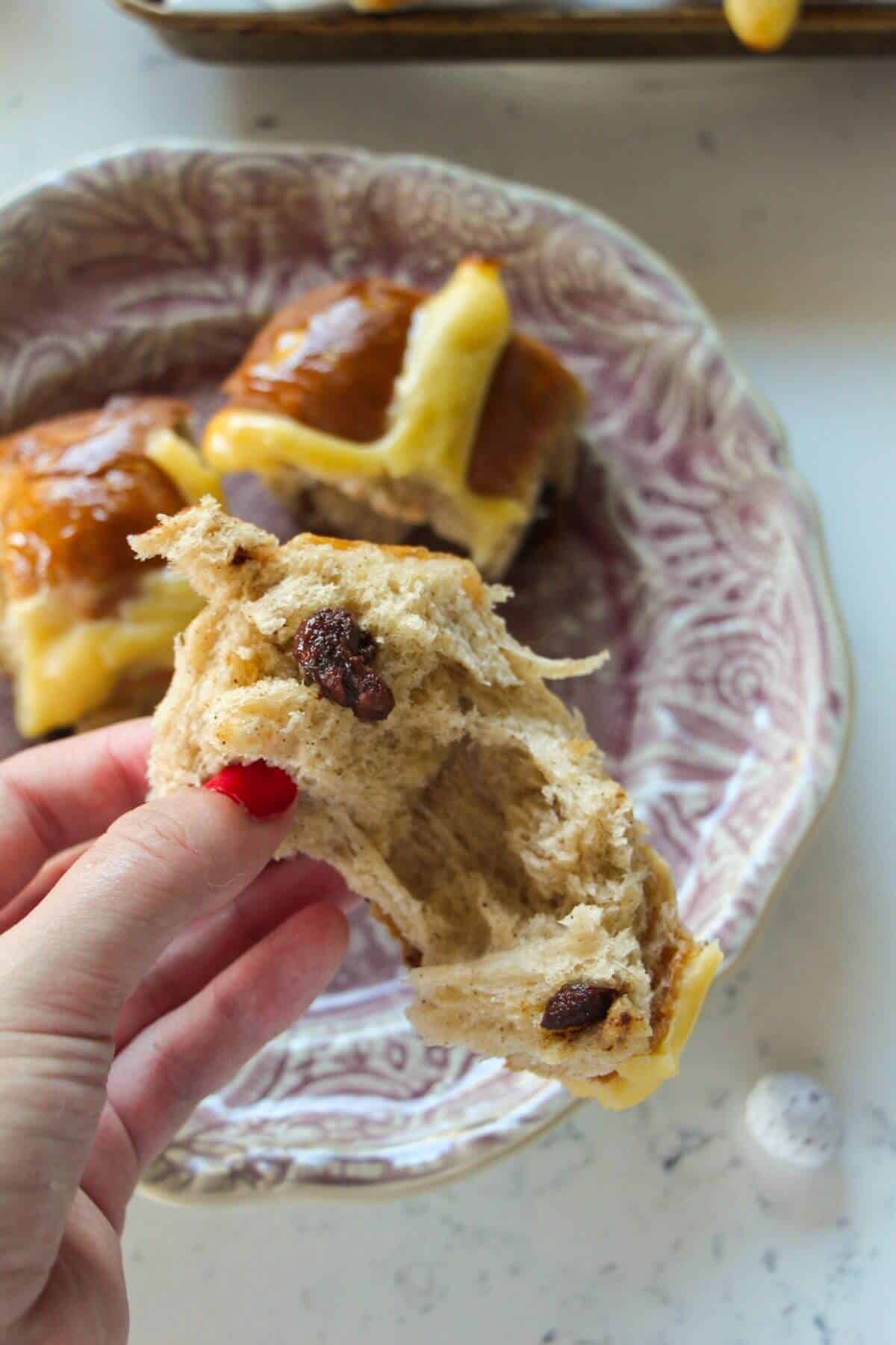 Hand holding a torn mini egg hot cross bun with another bun in the background.