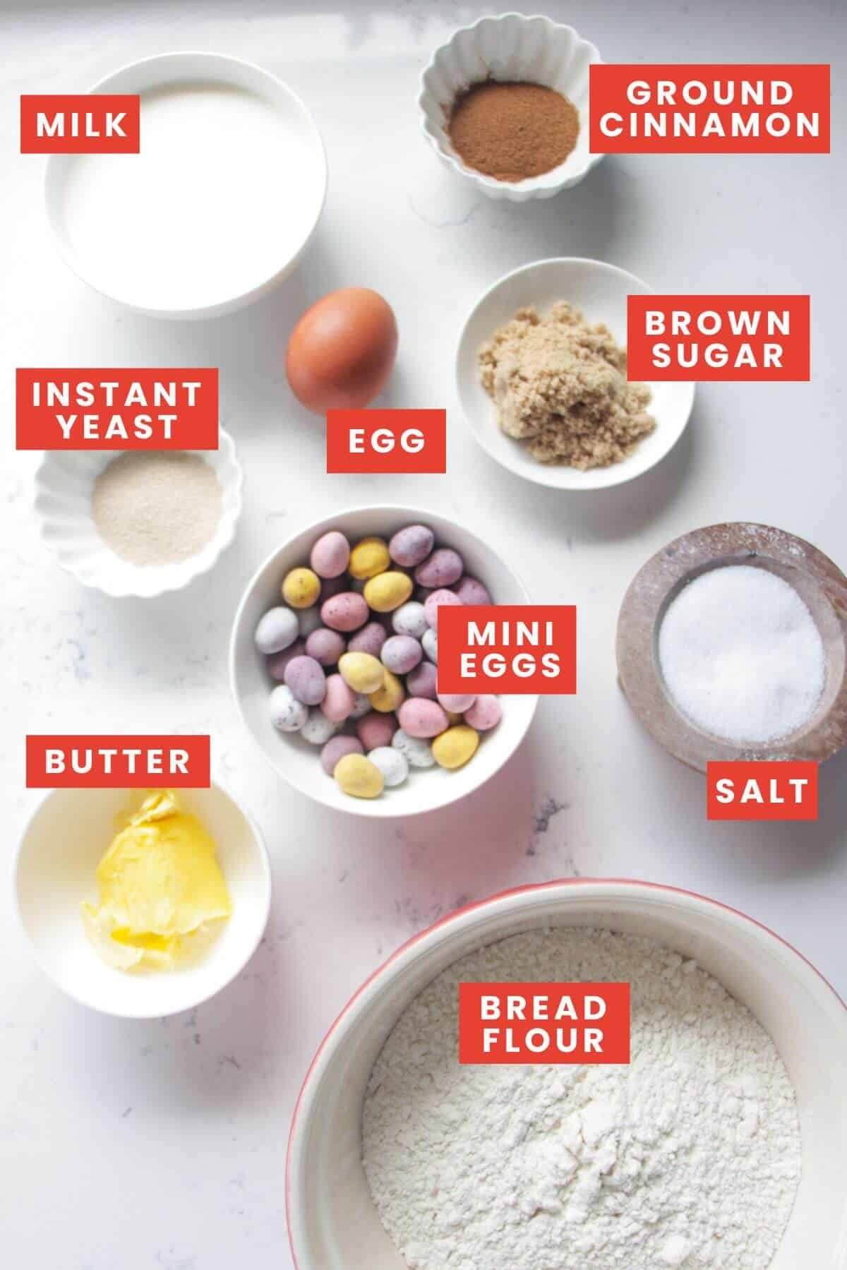 Ingredient for mini egg hot cross buns laid out on a white marble background and labelled.