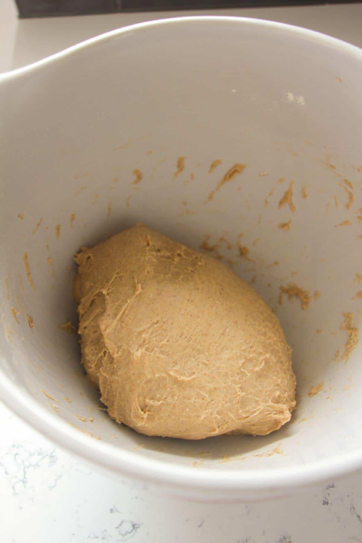 Hot cross bun dough after being kneaded in a large white bowl.