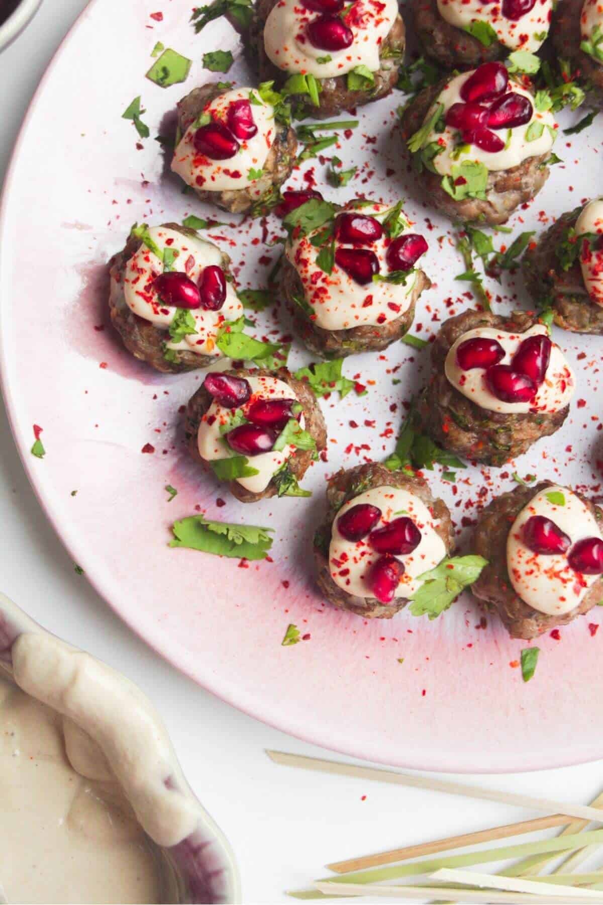 Close up of decorated lamb meatballs on a small pink plate.