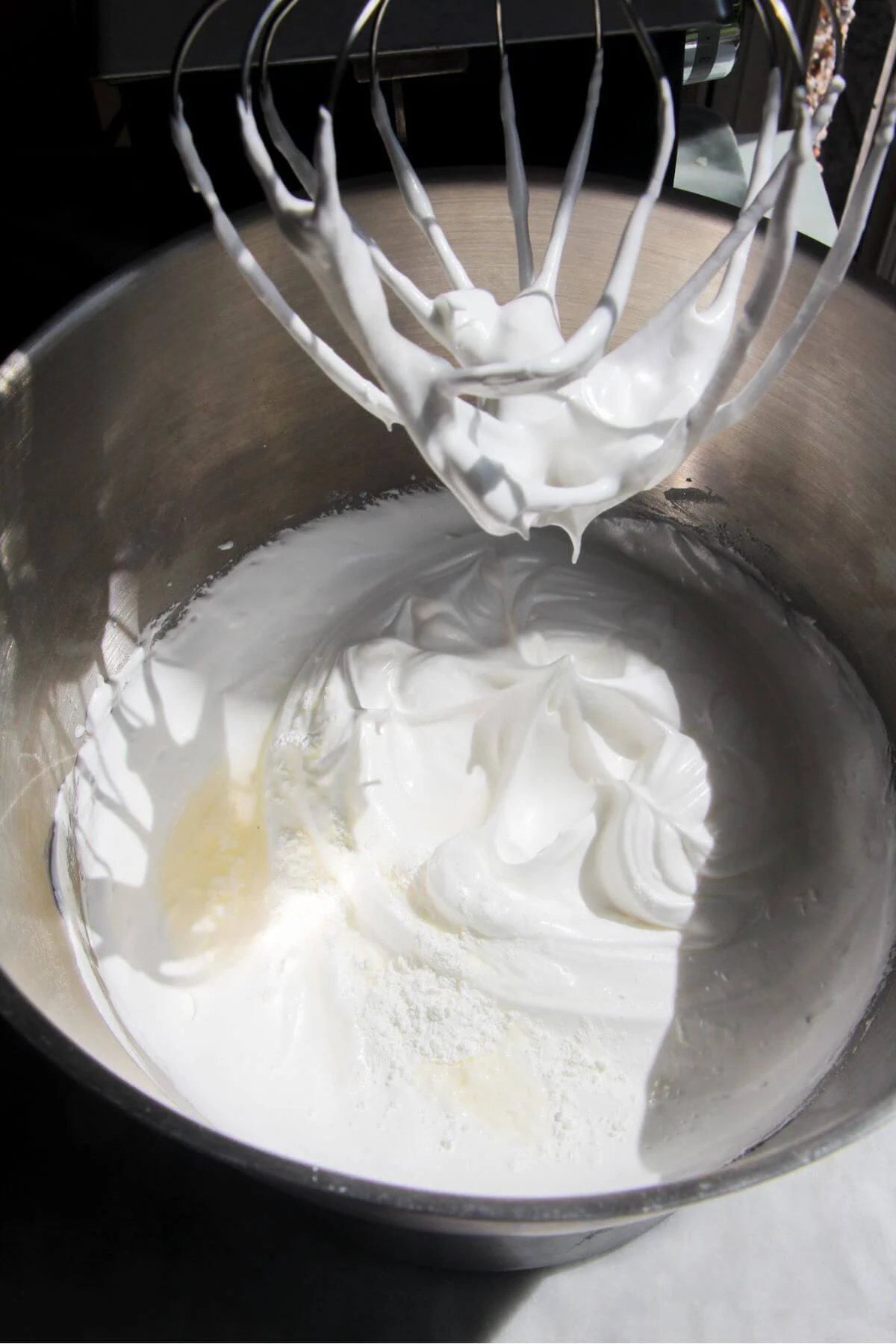 Vinegar and cornflour added to whipped meringue in a silver bowl.