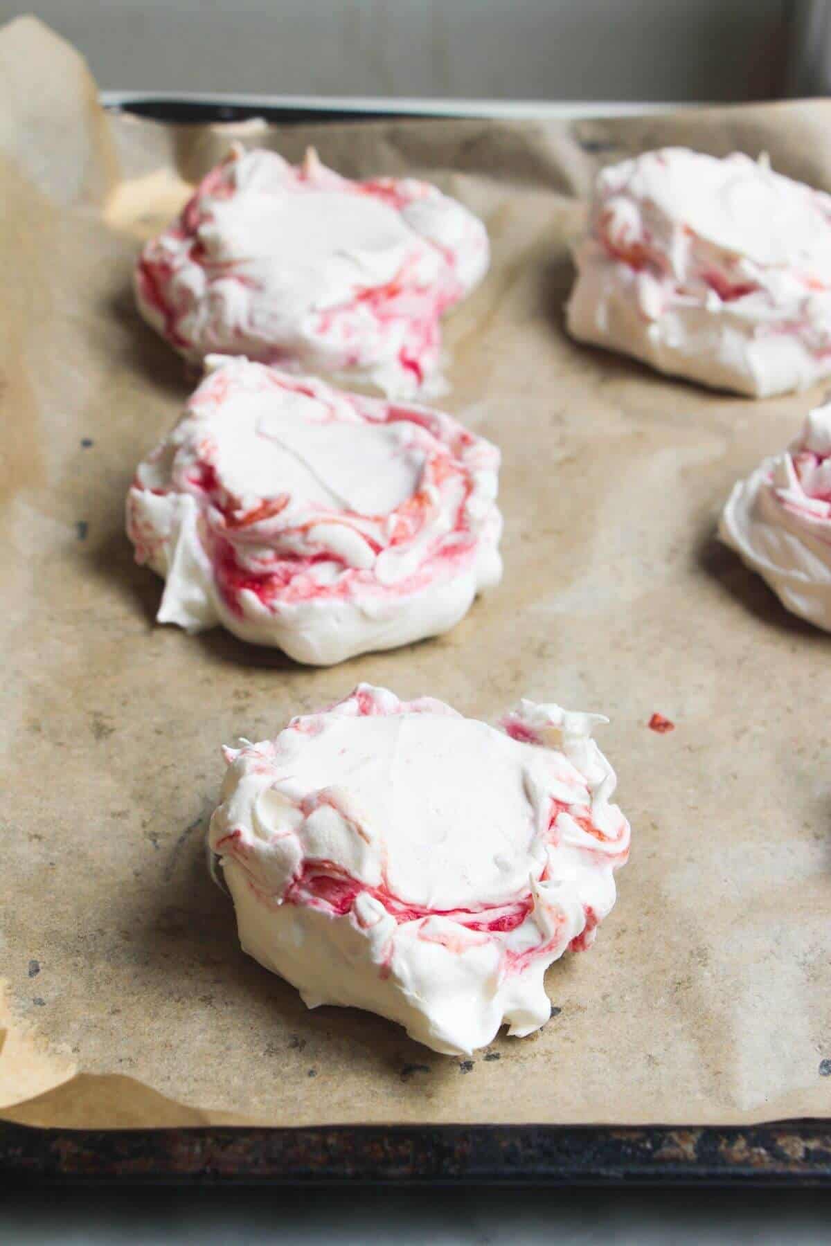 Close up of berry ripple pavlovas on a lined baking tray.