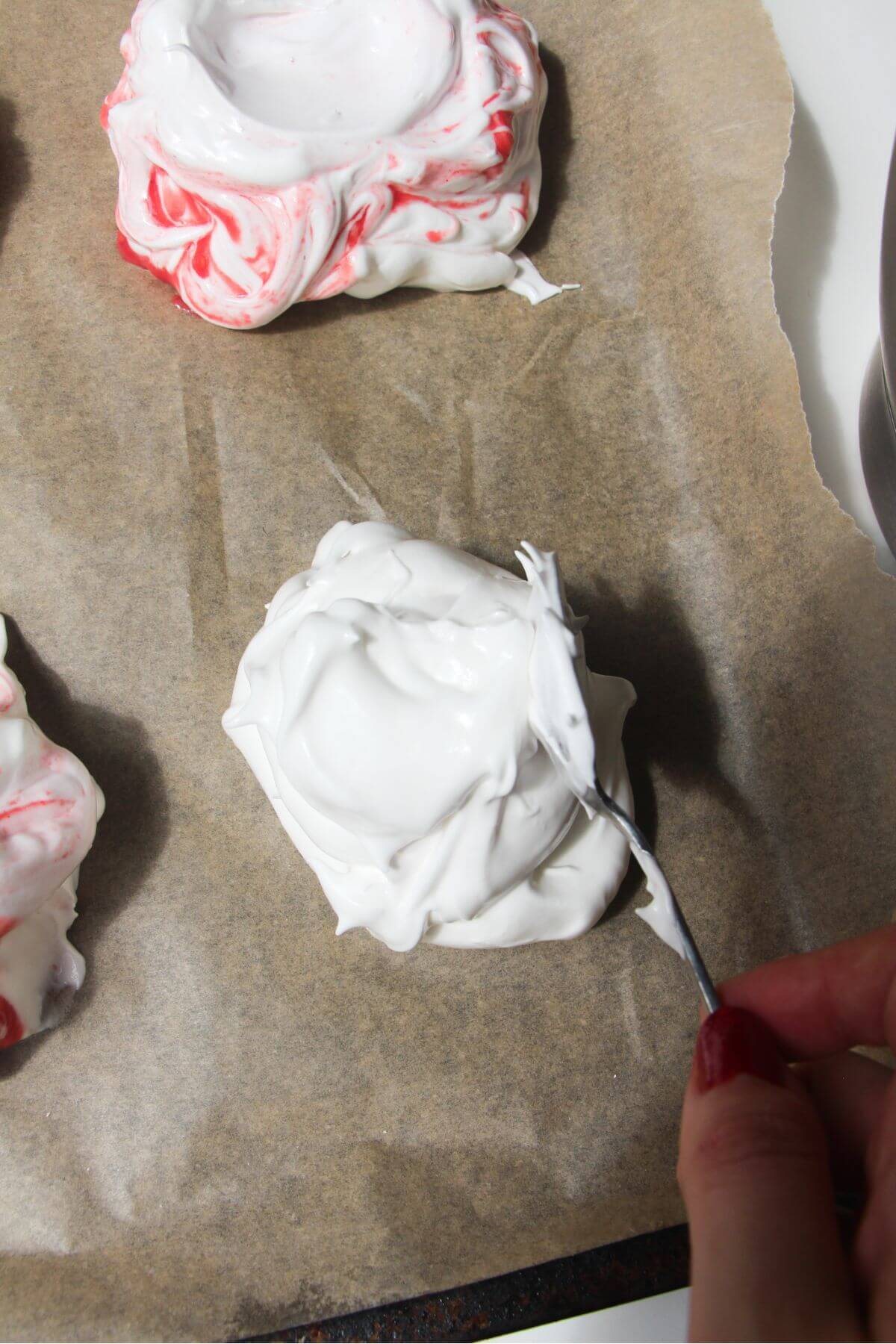 Silver spoon dolloping meringue onto lined baking tray.