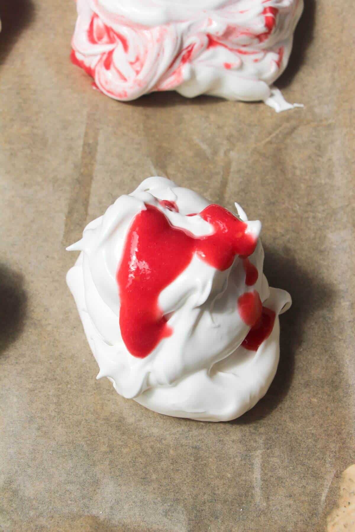 Raspberry puree drizzled on top of meringue on a baking paper lined tray.