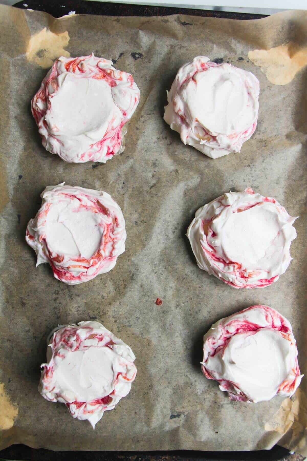 6 berry ripple mini pavlovas on a lined baking tray.