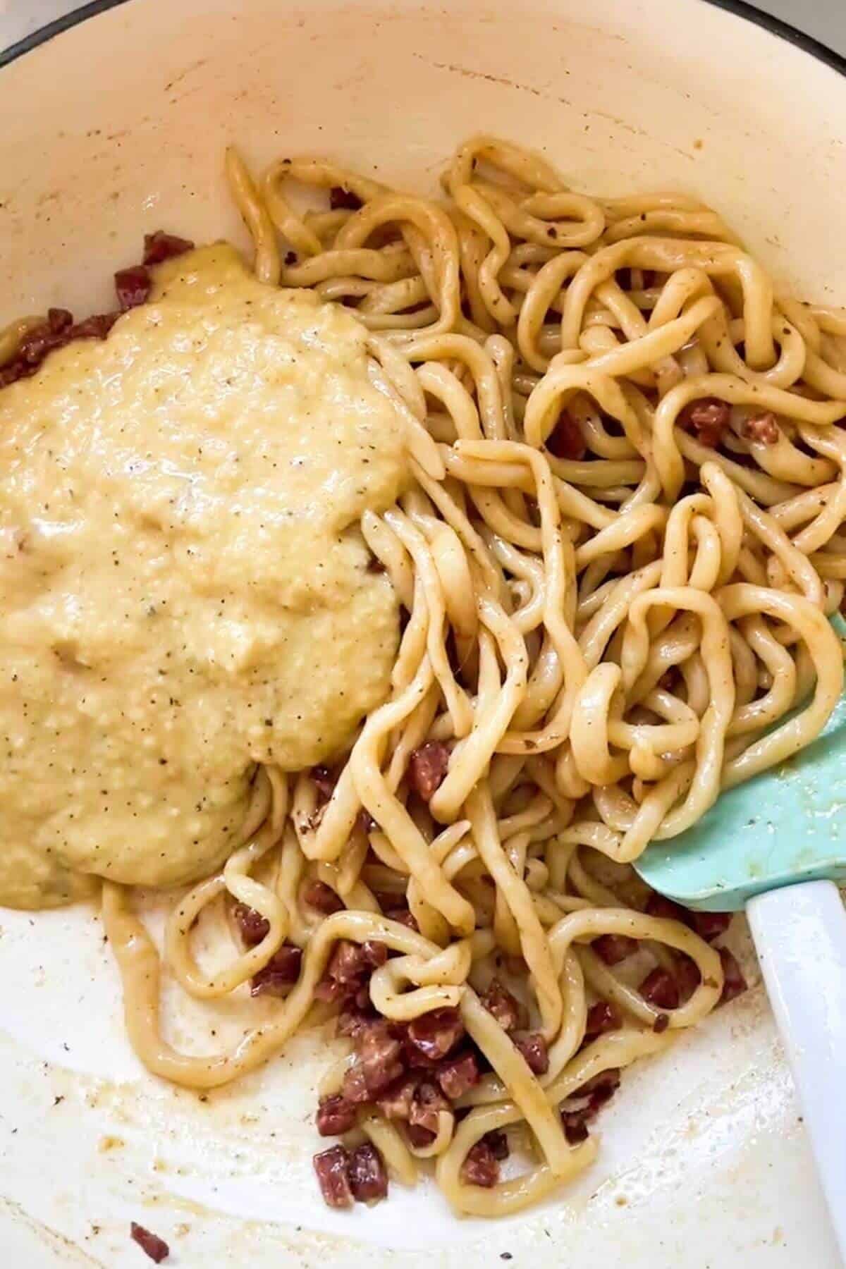 Tempered cheese and egg mix on top of spaghetti in a pan.