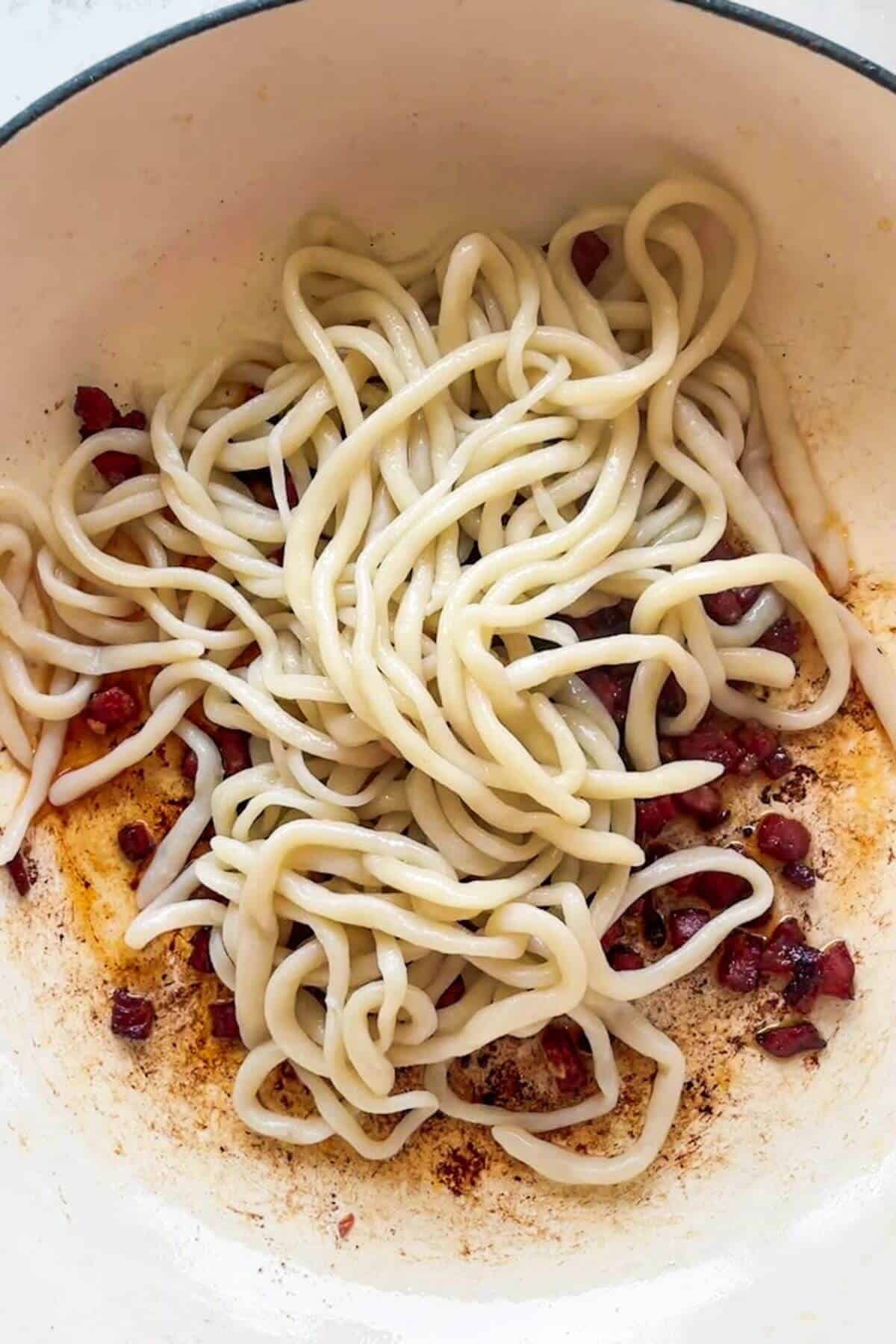 Cooked spaghetti added to pan with crispy guanciale.