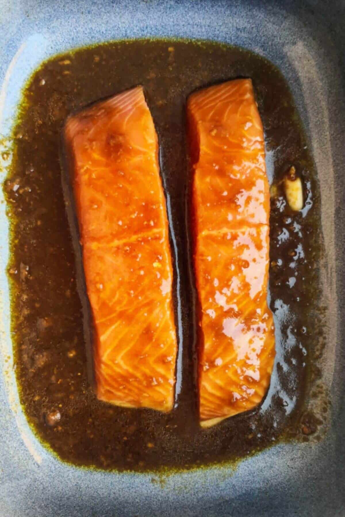 2 salmon fillets in a blue oven dish with miso marinade over the top.