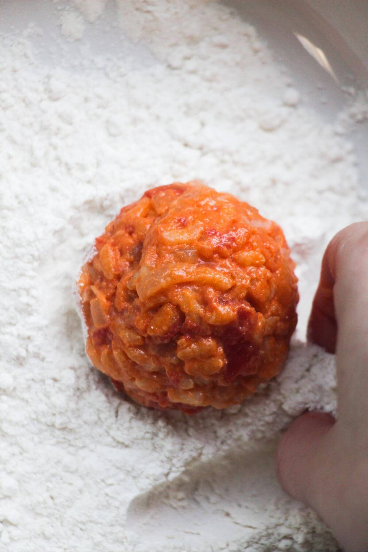 Close up of arancini ball in a bowl of flour about to be coated.