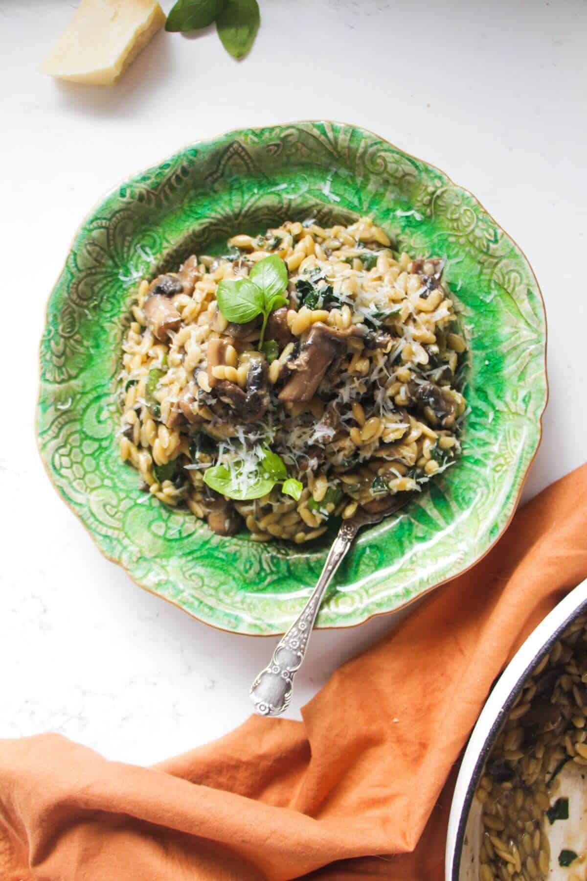 Mushroom orzo on a small green plate with a small spoon in it.