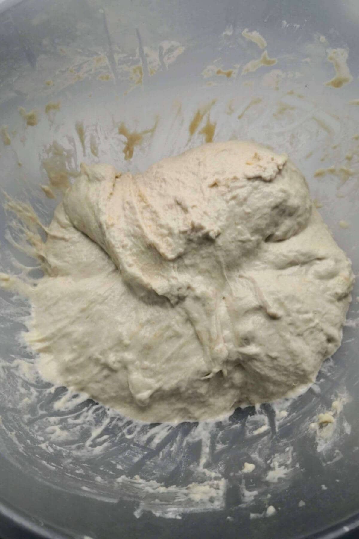 Focaccia dough in a large clear mixing bowl with a rough top.