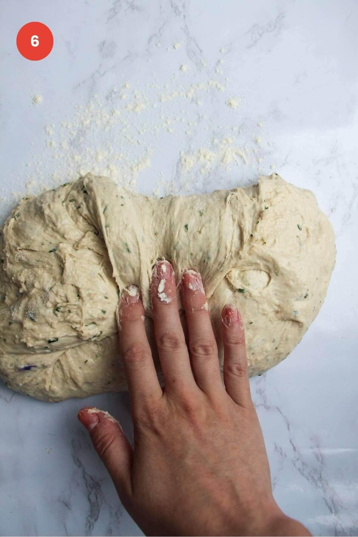Hand folding bread dough over itself.
