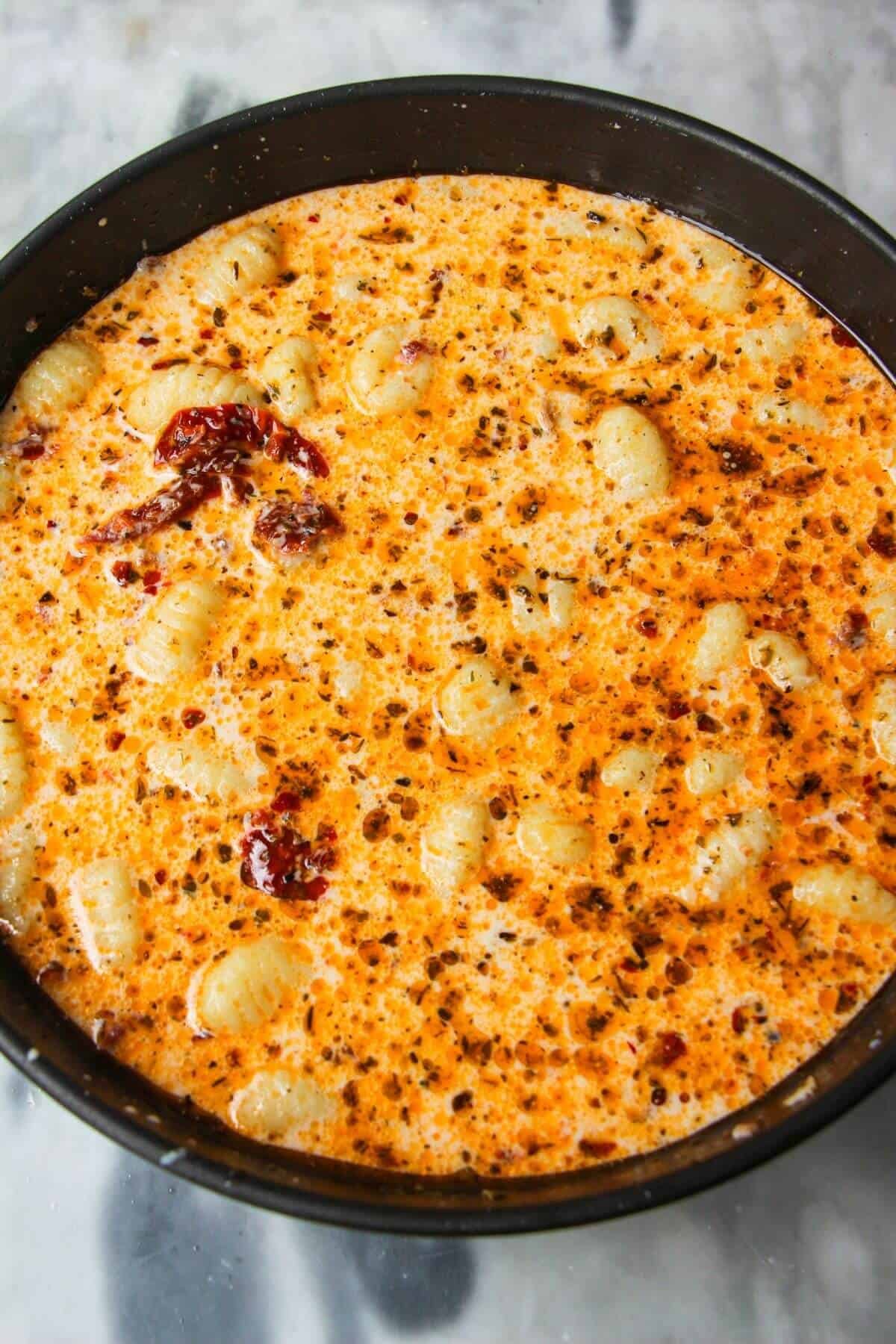 Gnocchi stirred through creamy sundried tomato sauce in a small black pan.