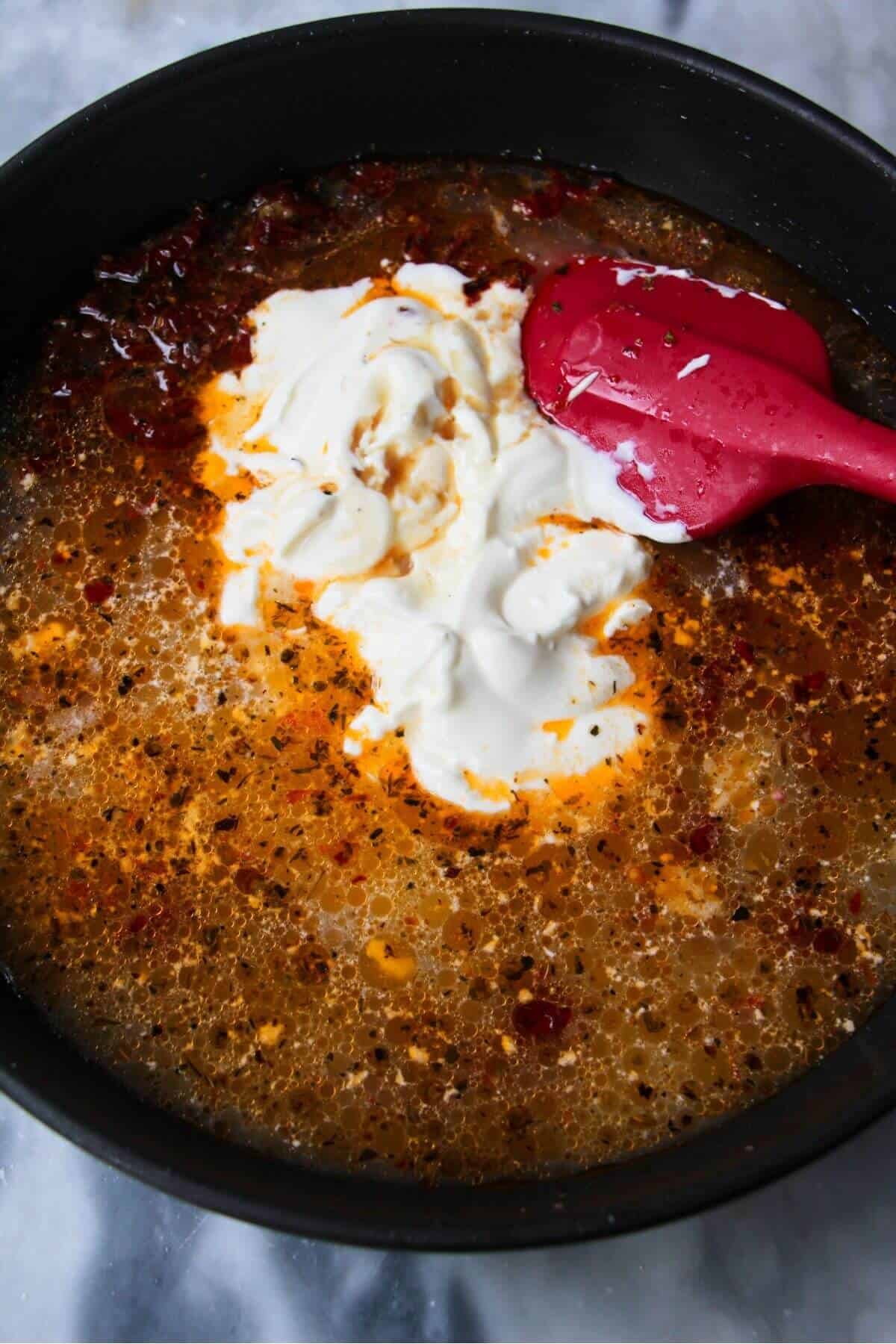 Sour cream added to stock and aromatics in a black pan.