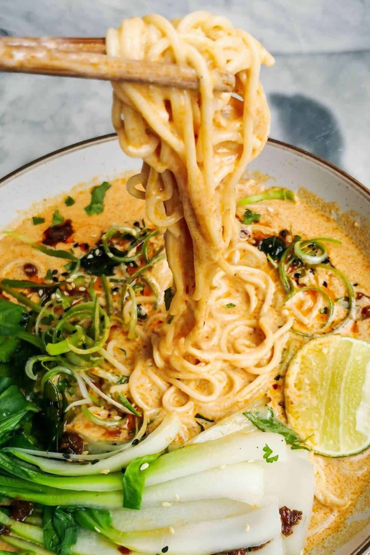 Chopsticks pulling up saucy coconut noodles in a white bowl.