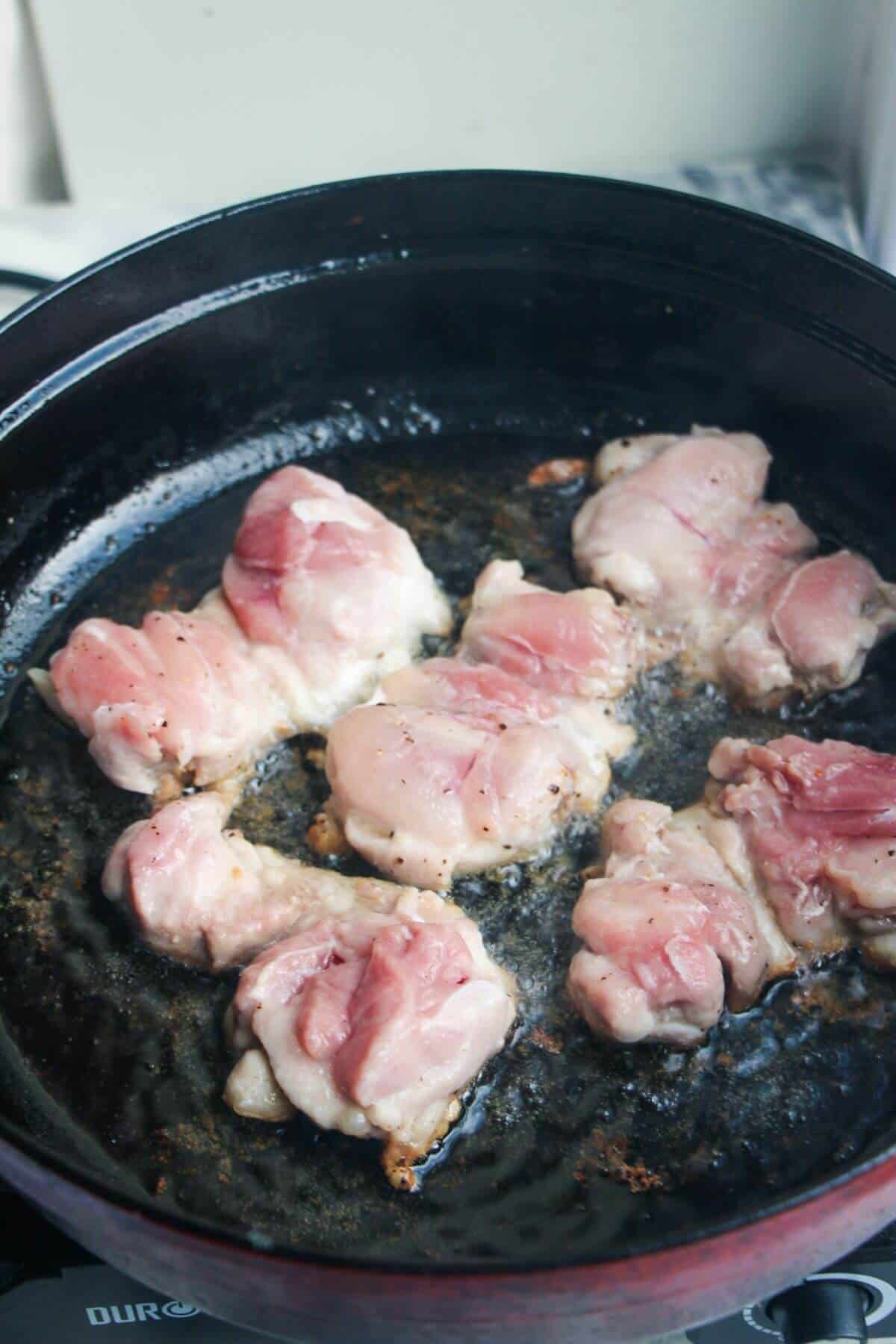 Five chicken thighs cooking in a large black pan.