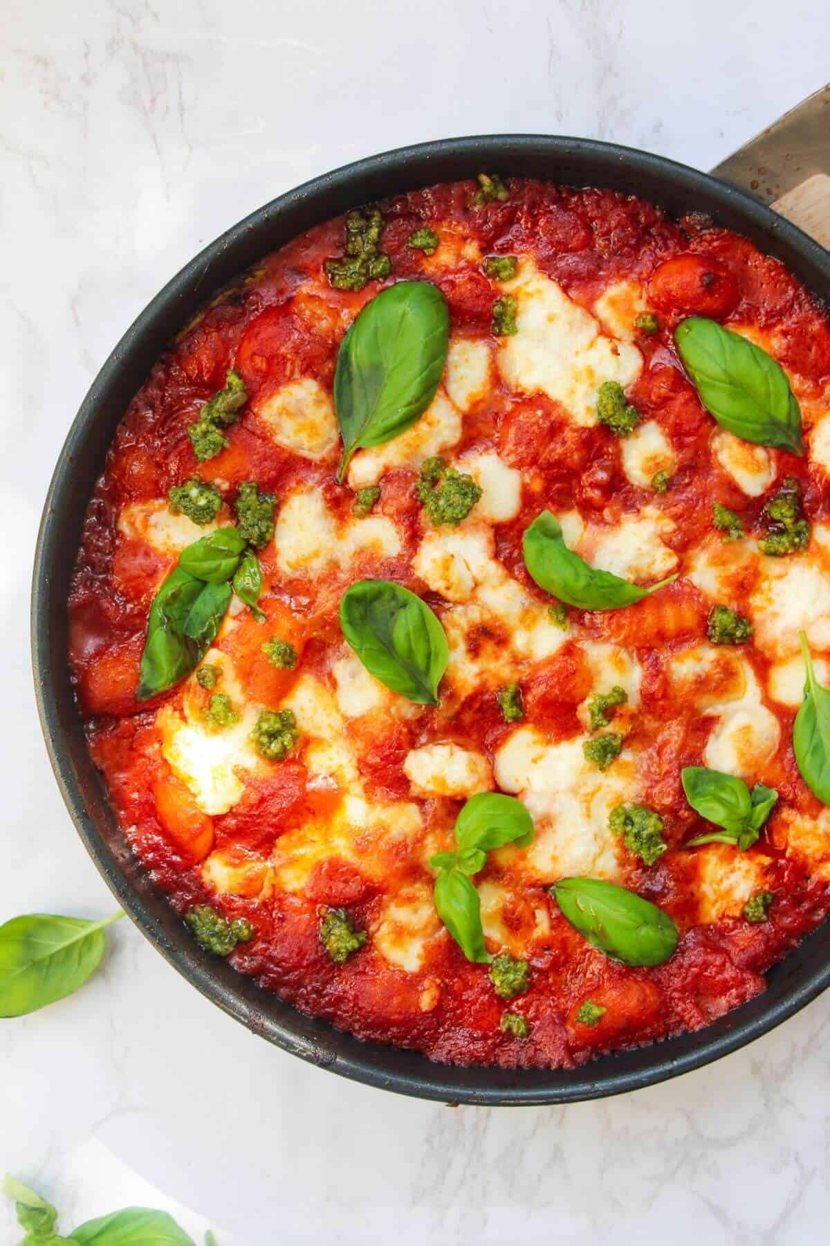 Mozzarella topped gnocchi alla sorrentina in a small frying pan, topped with basil leaves.