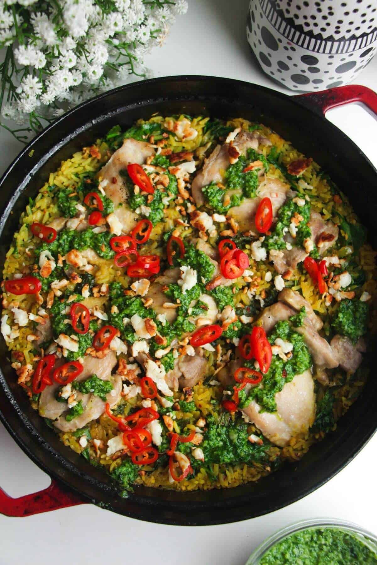 Pesto topped golden chicke and rice in a large pot.