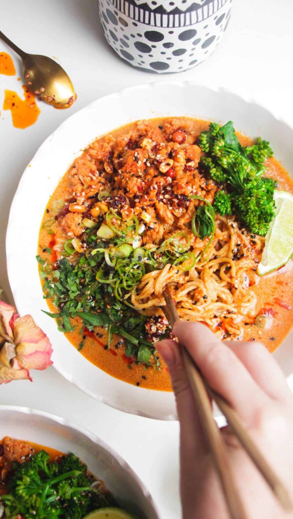 Hand with chopsticks with a bowl of peanut butter noodles.