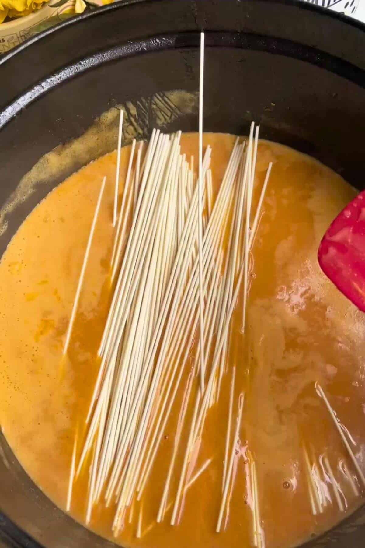 Noodles added to coconut peanut sauce in a pot.