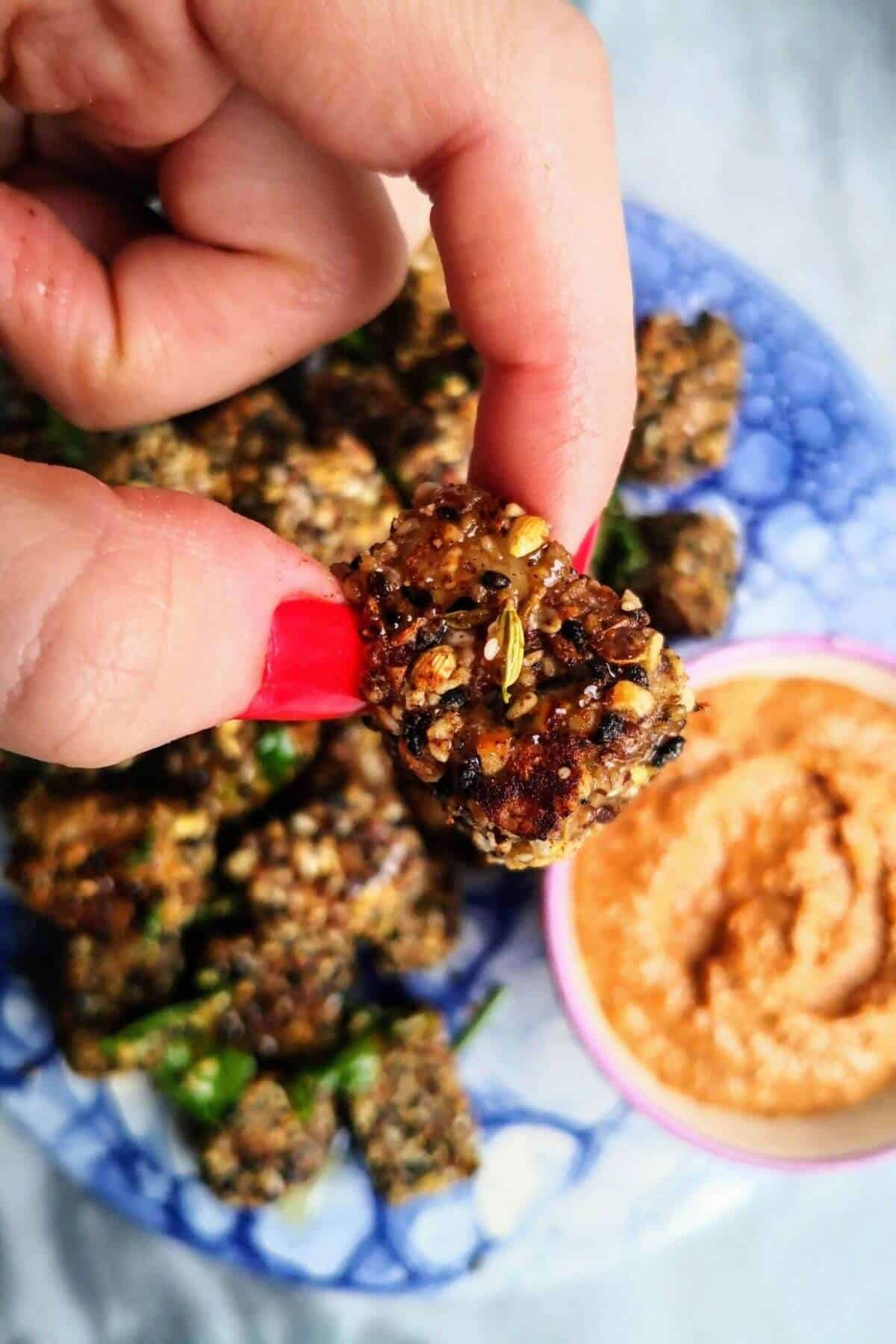 Hand holding a halloumi bite with plate of bites in the background.