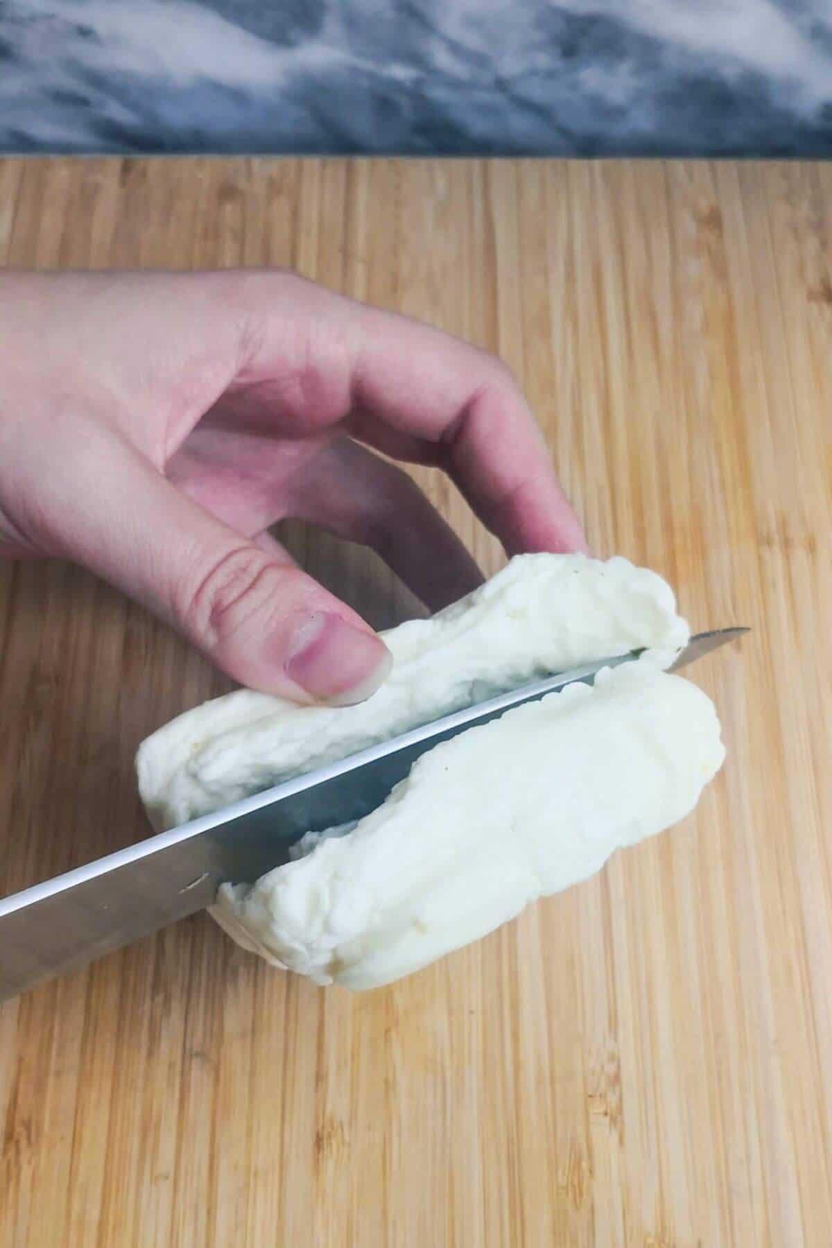 Cutting halloumi block in half on a wooden board.