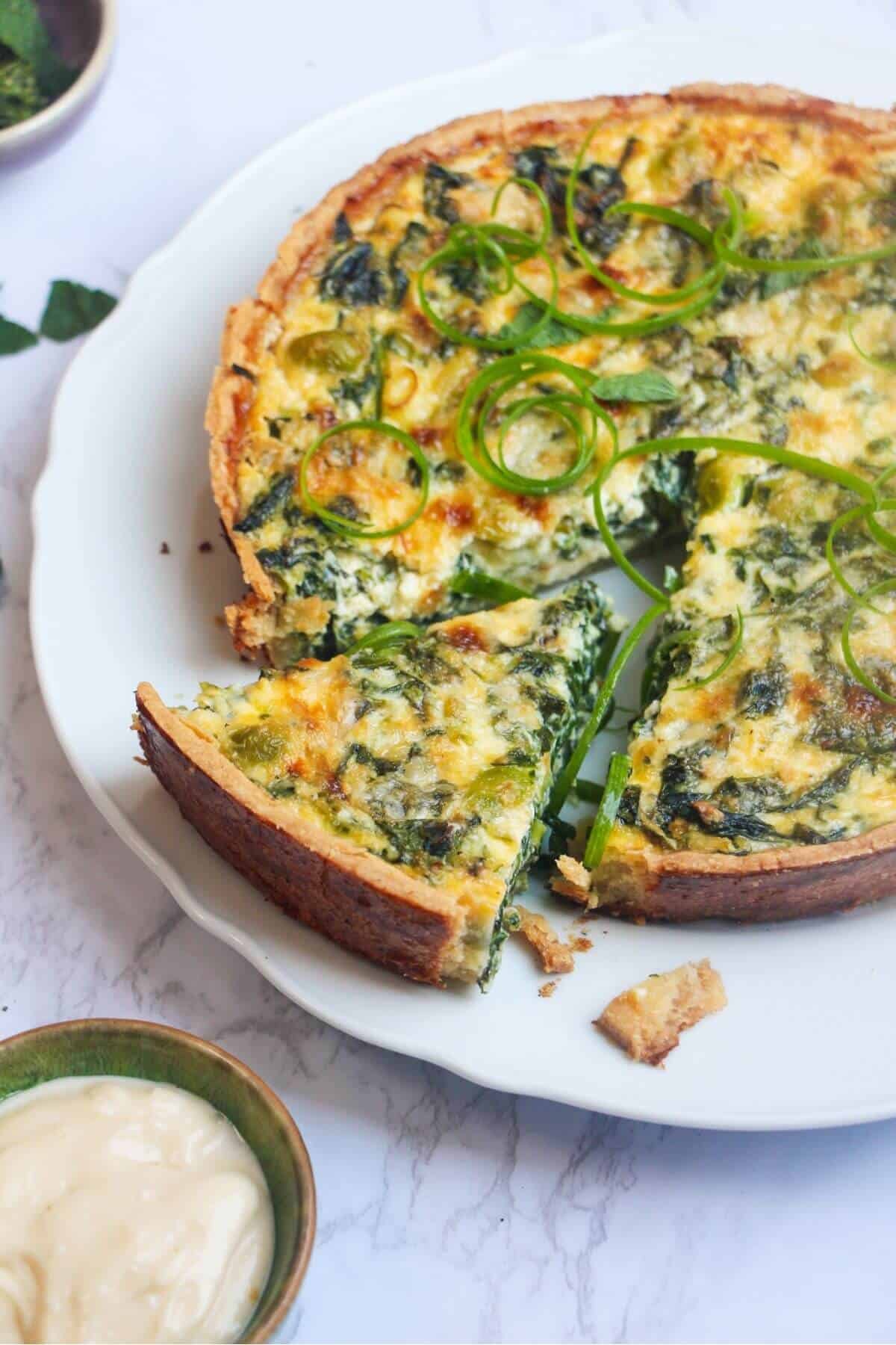 Coronation quiche on a scalloped white plate with a piece cut out of it.