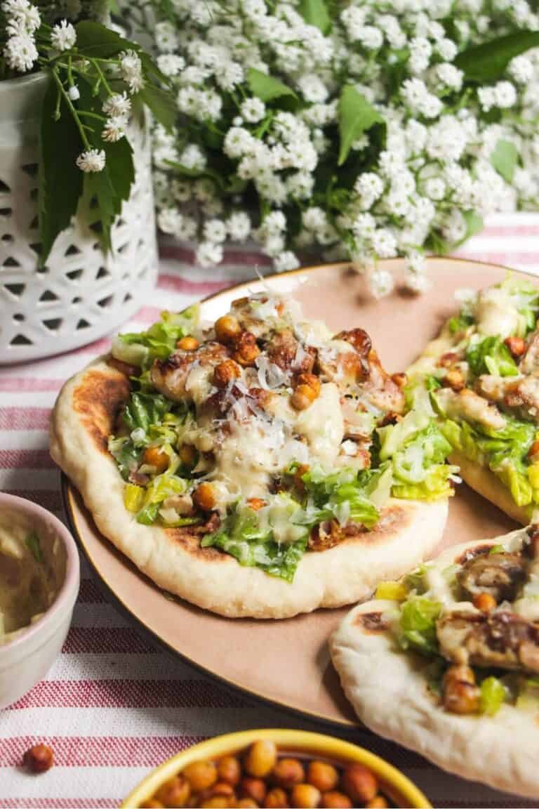 Flatbread on a plate topped with Caesar salad, charred chicken pieces and creamy Caesar dressing.