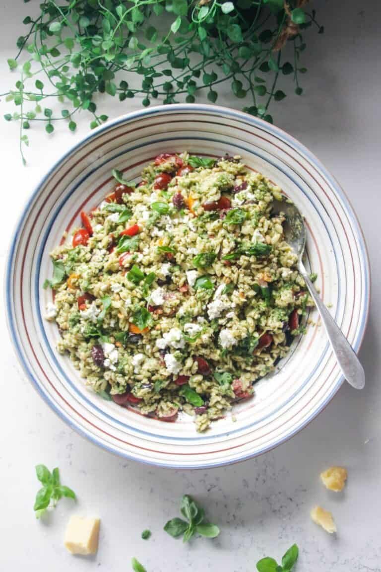 Orzo pesto salad in a large colourful serving bowl with a silver spoon.