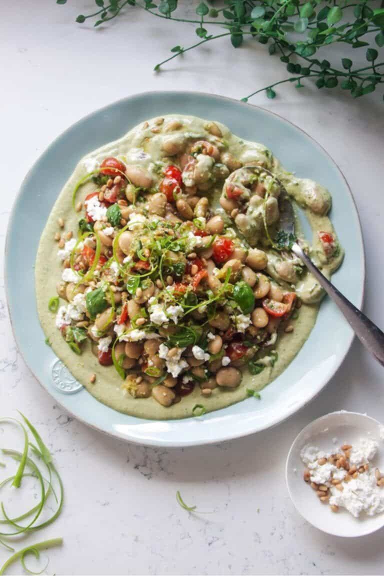 Mediterranean white bean salad on whipped basil tahini on a large light blue serving plate.