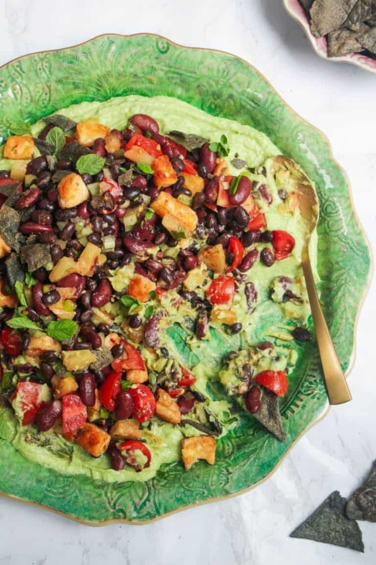 Mexican bean salad on top of whipped avocado on a large green platter.