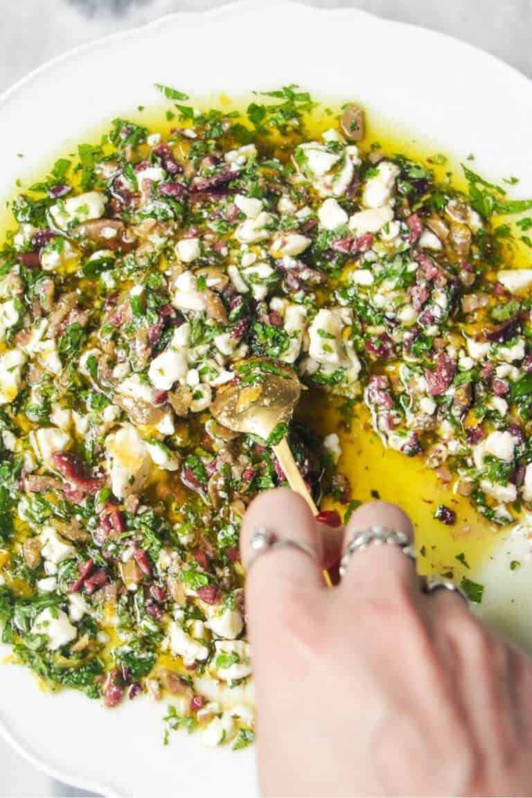 Hand mixing ingredients for Greek dipping oil in a large white plate.