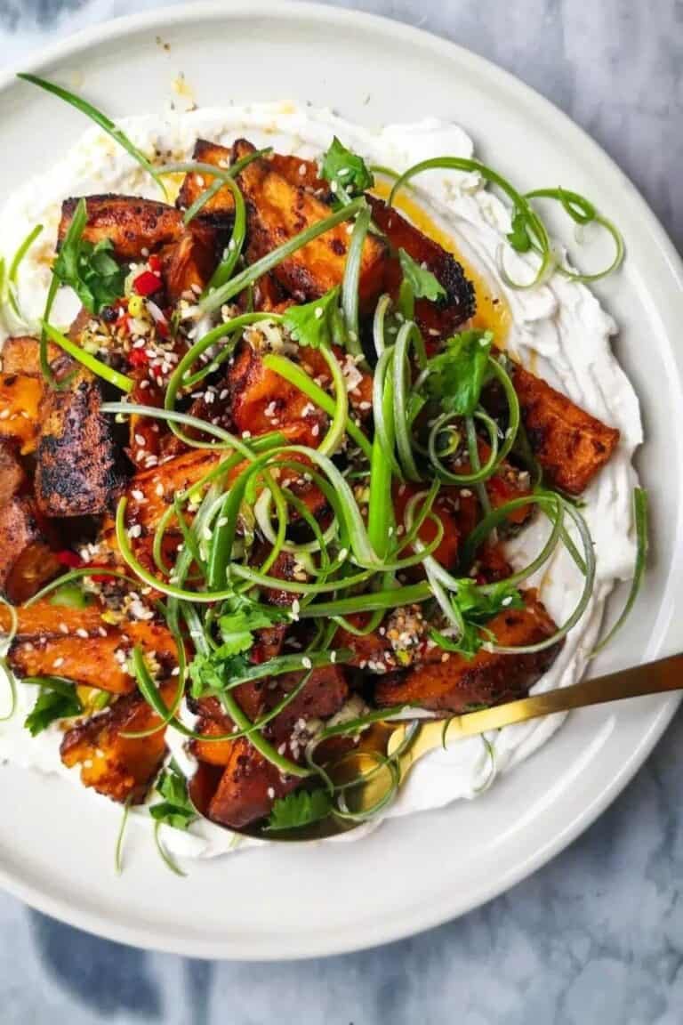 Miso roasted sweet potatoes on labneh, with chilli lime salsa on top on a white plate.