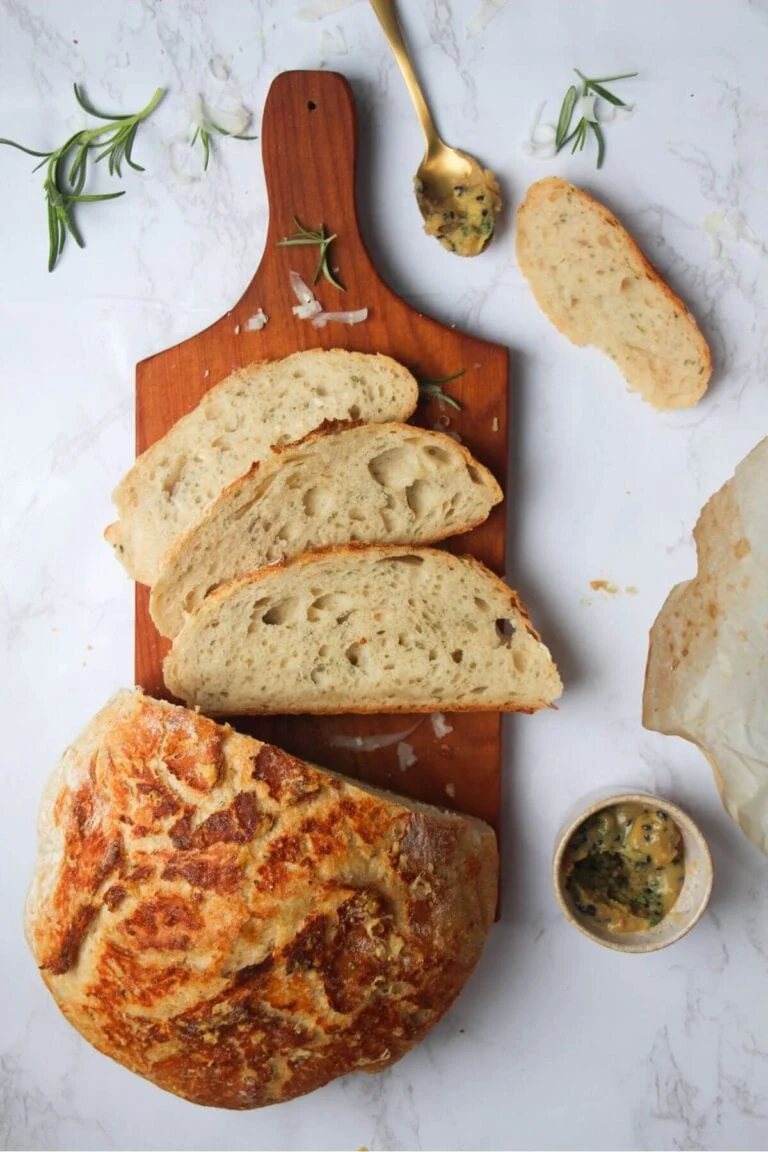 3 slices of bread on a small wooden board with the rest of the loaf and garlic butter in the background.
