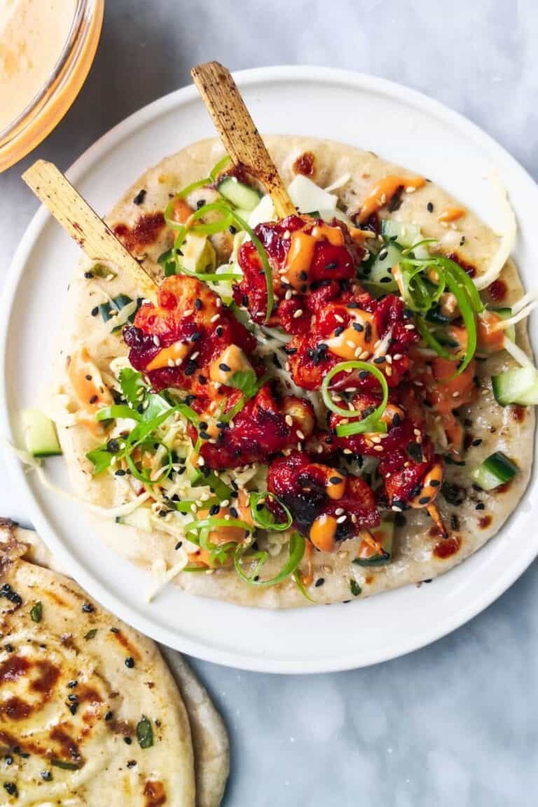 2 gochujang chicken skewers on top of slaw, on a flatbread on a white plate, with flatbreads and gochujang aioli on the side.